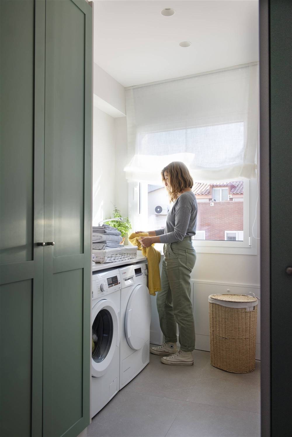 mujer recogiendo ropa de la colada junto a una lavadora 00532170 O