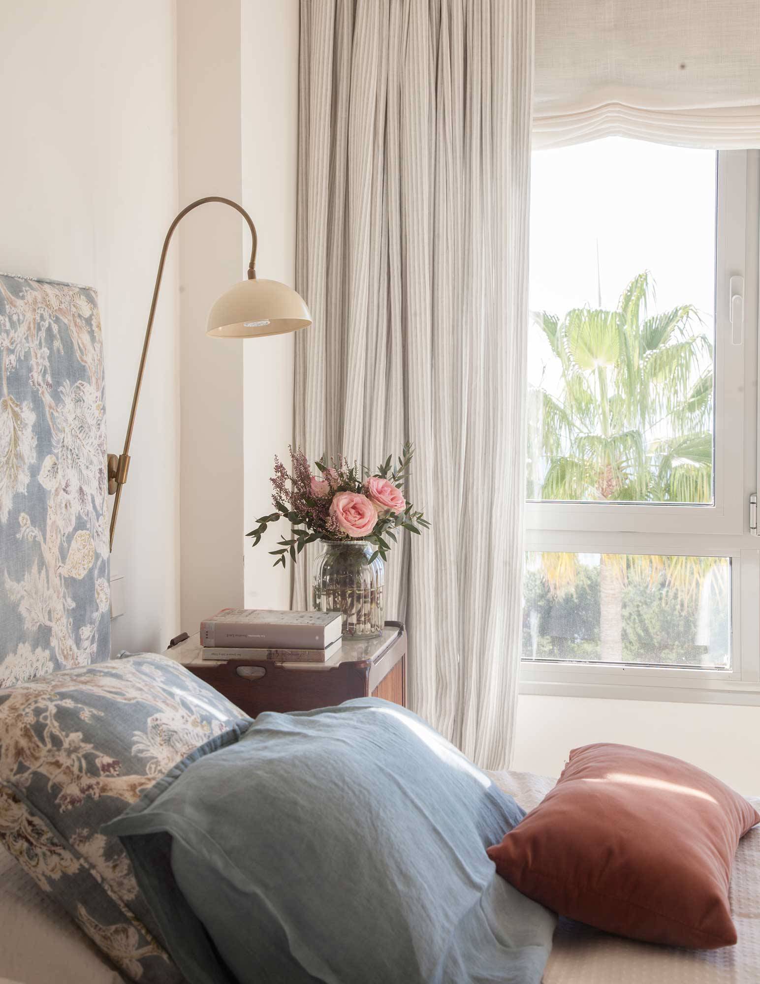 Dormitorio pequeño con cortinas con rayas y cabecero tapizado con estampado floral. 