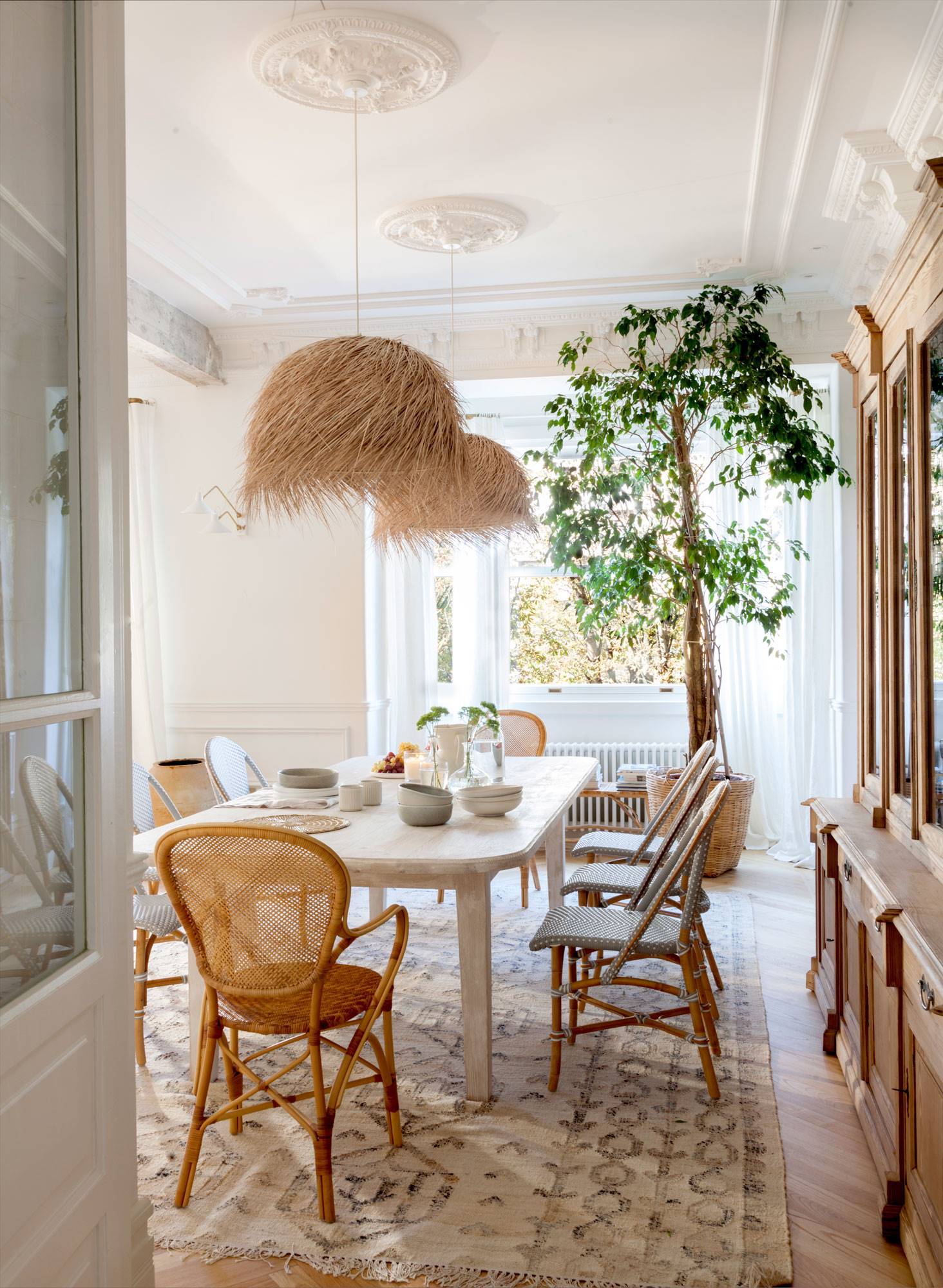 Comedor con techo clásico con molduras y rosetones y muebles de fibras naturales. 