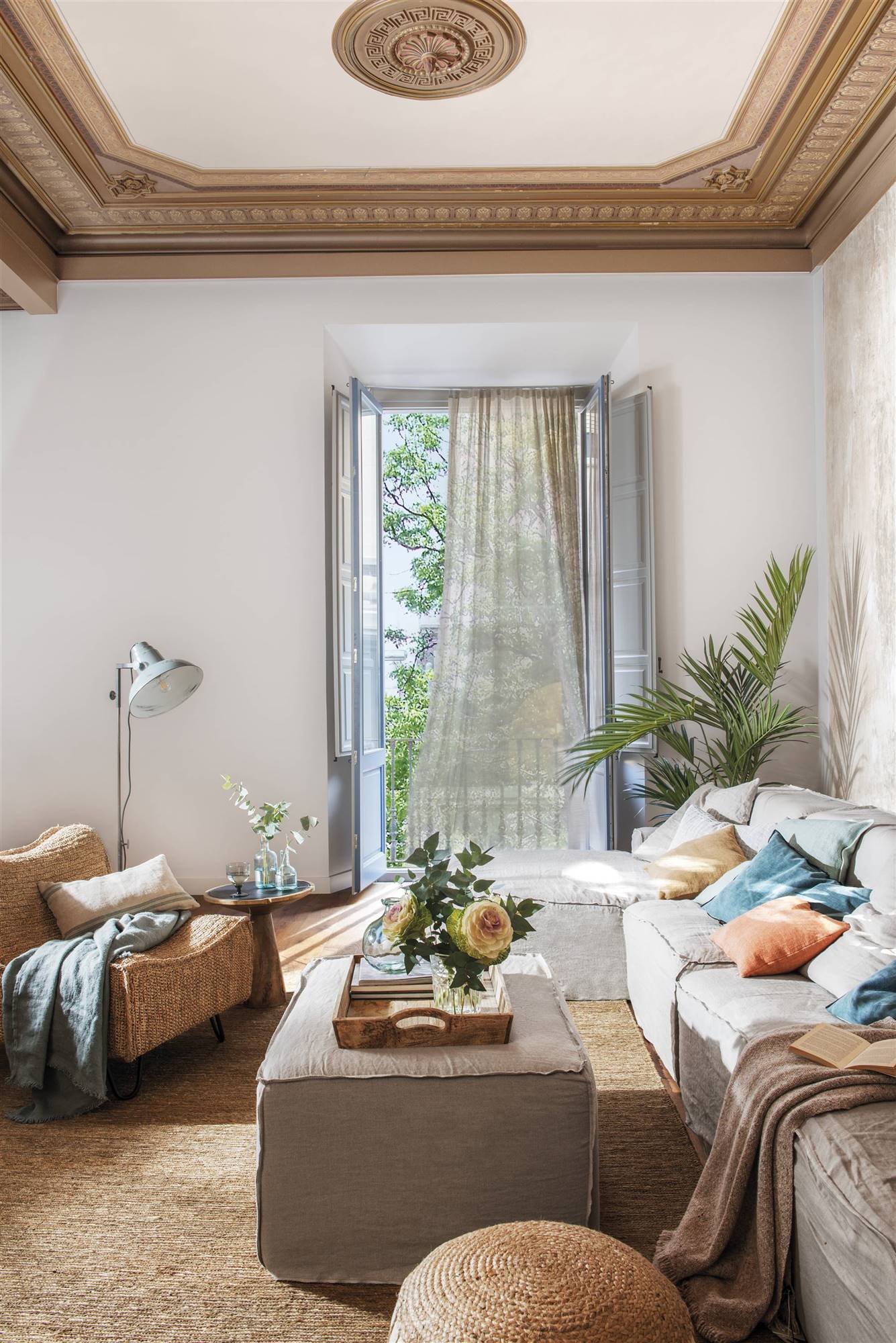 Salón con techo con molduras, sofá y mesa de centro de lino y butaca. 