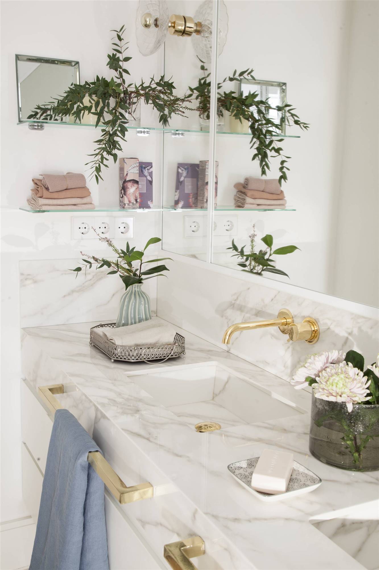 Baño con encimera de mármol blanco, detalles dorados y estantes de cristal