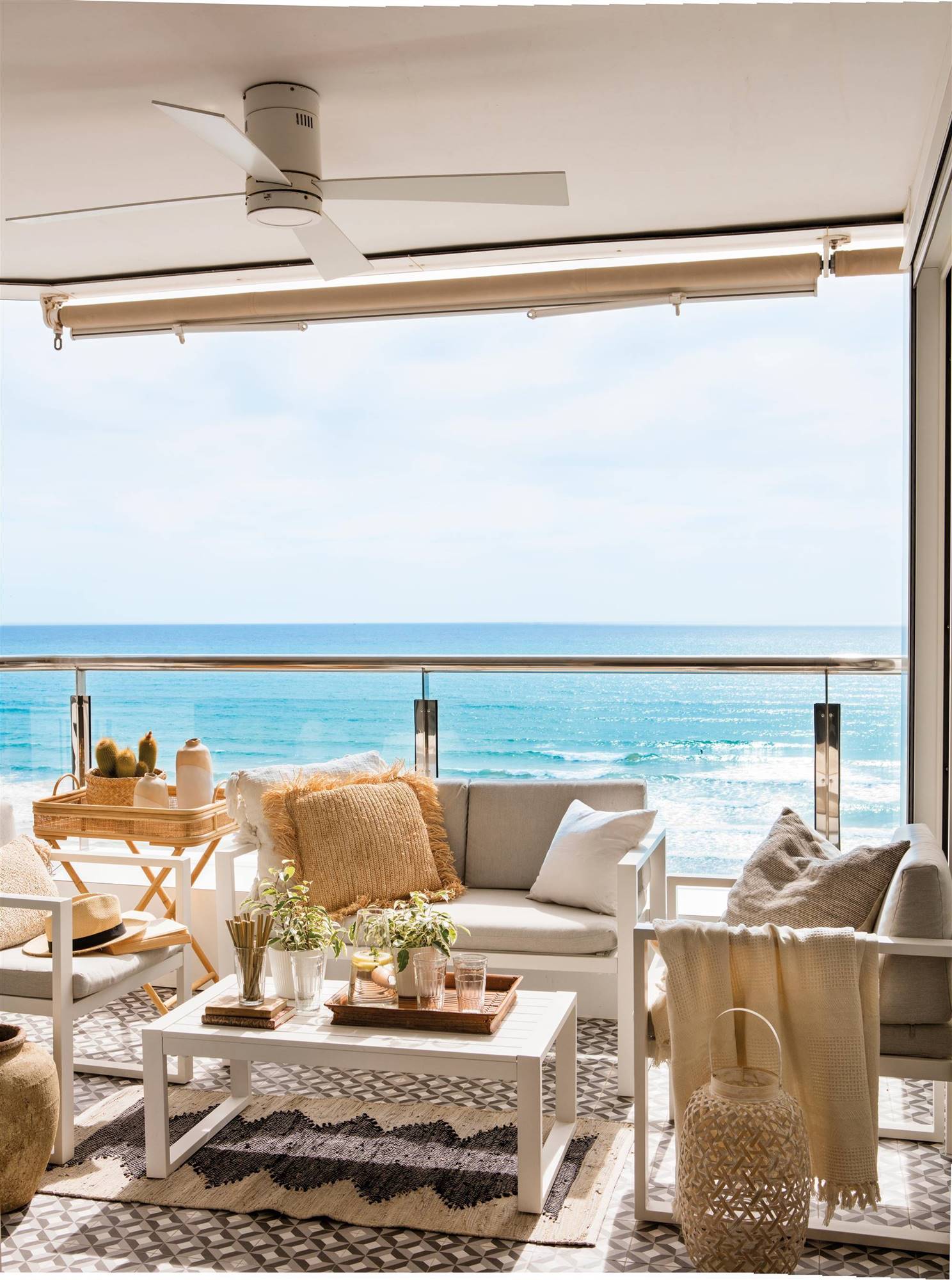 Terraza con salón exterior con vistas al mar y barandillas de cristal. 