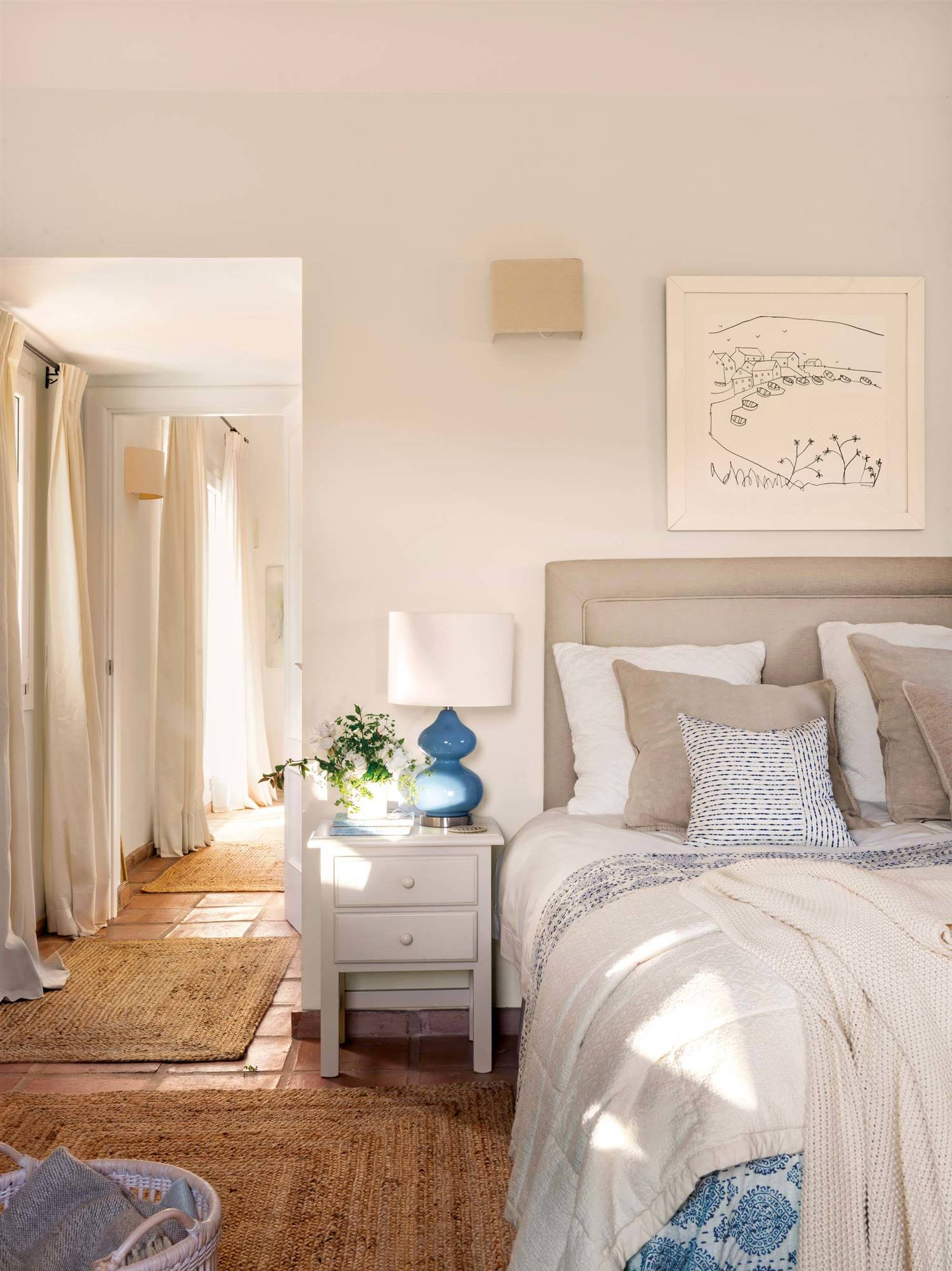 Dormitorio rústico decorado en blanco y azul, con suelo de barro y alfombras de fibra vegetal.