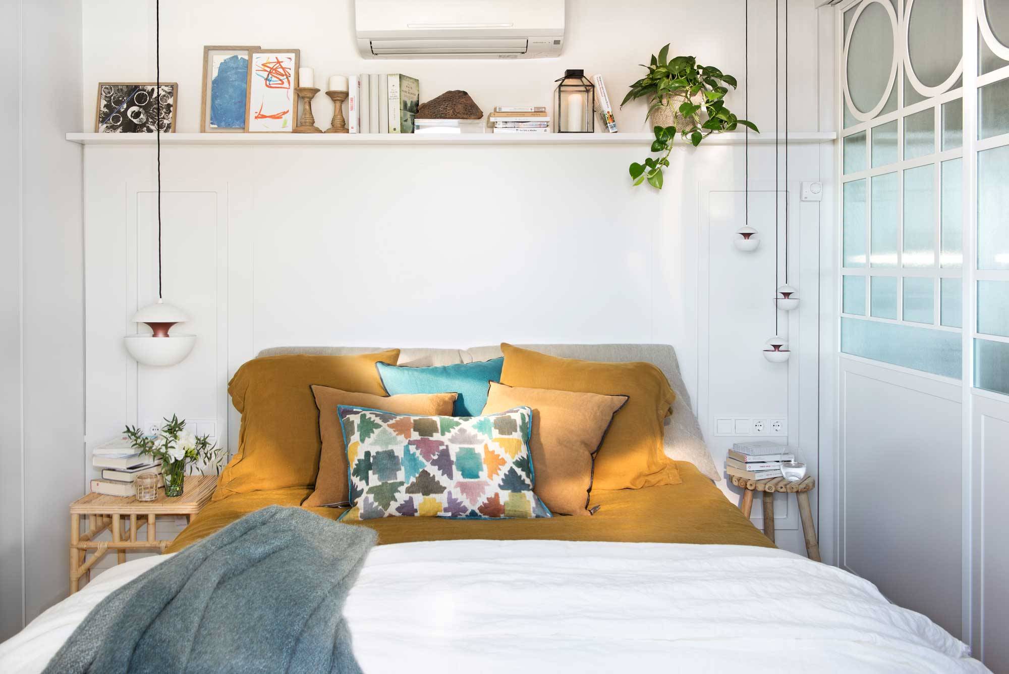Dormitorio pequeño con ropa de cama de color mostaza y un estante en la pared del cabecero.. 