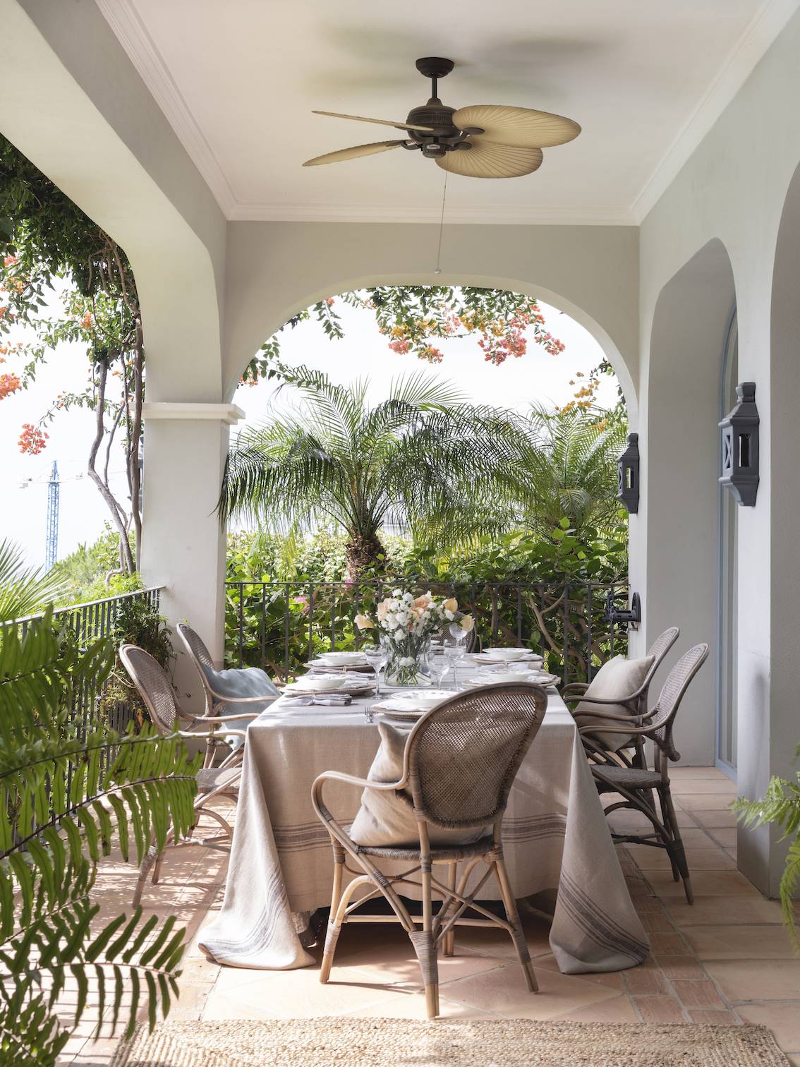 Comedor exterior de estilo colonial en tonos claros rodeado de plantas de exterior.