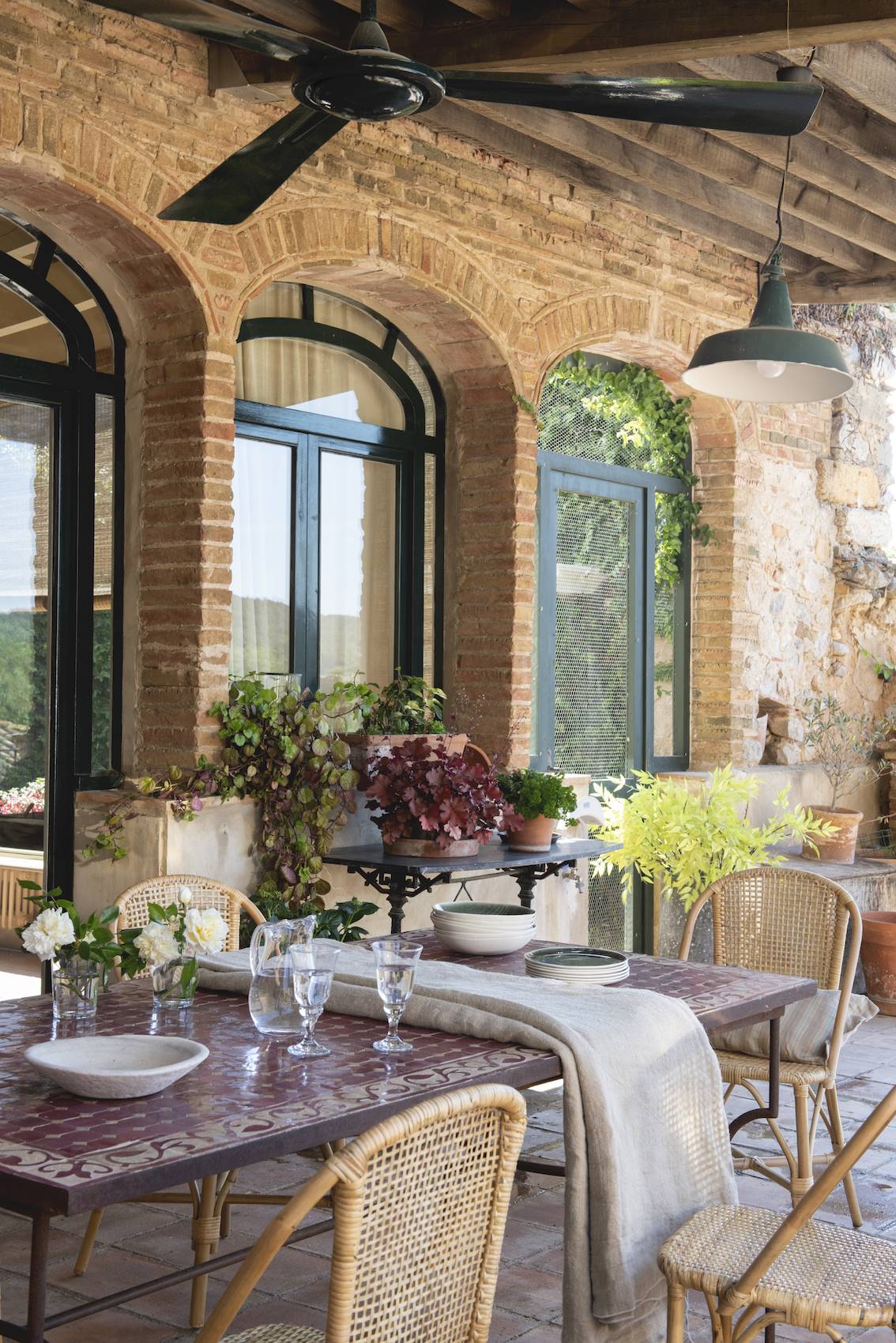 Comedor exterior con aire industrial y una gran mesa de jardín de mosaico de piedra. 