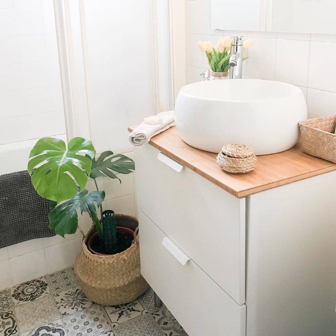 Mueble de baño suspendido en color blanco con encimera de madera y planta monstera en cesta de fibras.