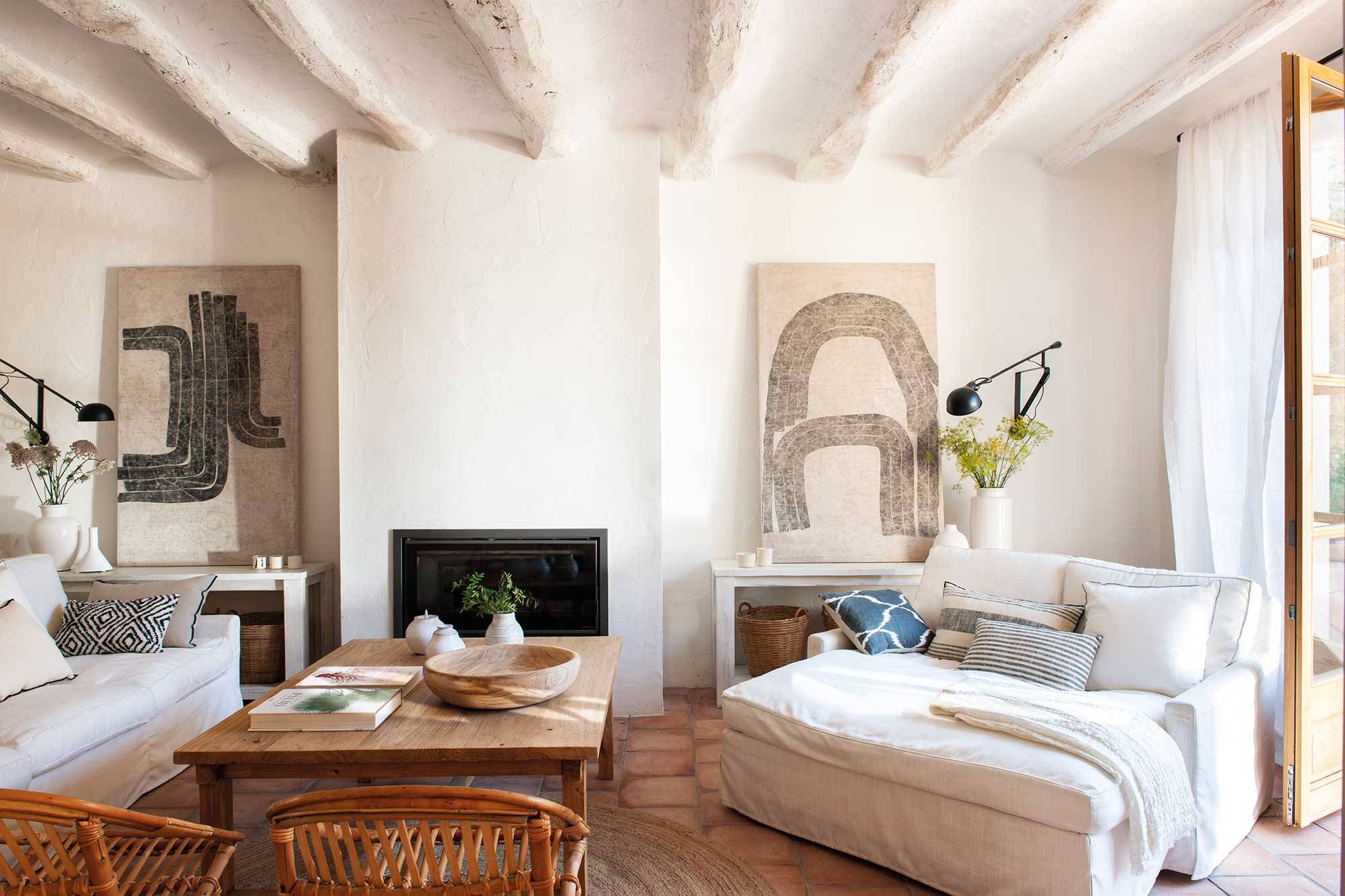 Salón nórdico con vigas blancas en el techo, chaise longue y cuadros de Walter Arias.