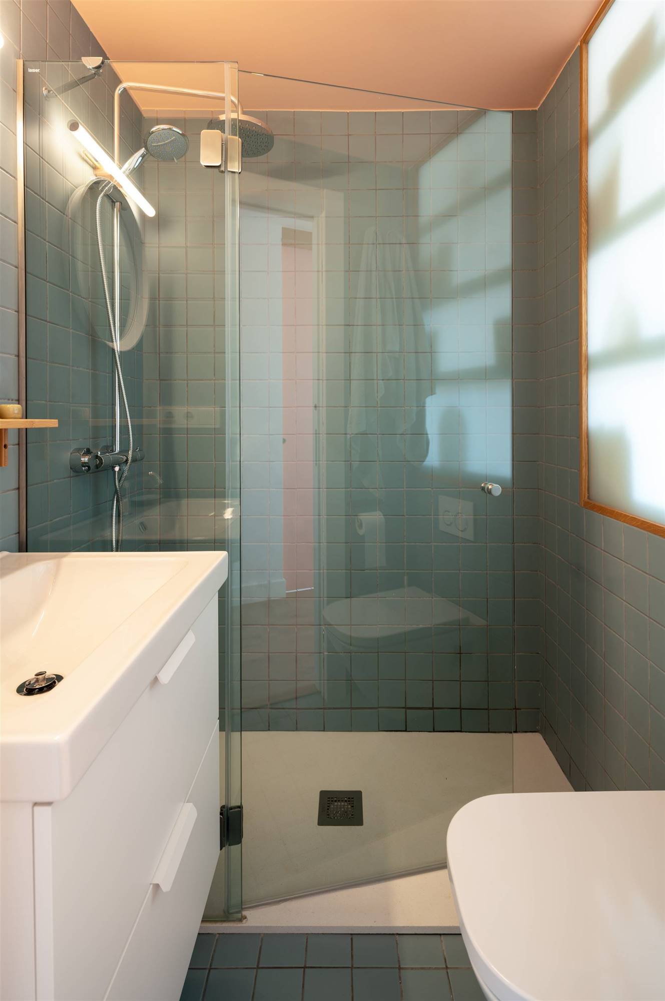 Un pequeño baño revestido con pequeña baldosas en tonos azules y con una ducha con mampara de cristal
