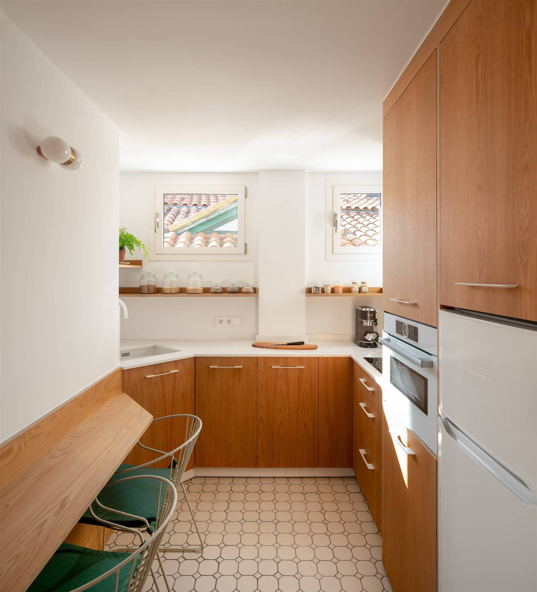 Una pequeña cocina en tonos blancos y madera con dos grandes ventanas 