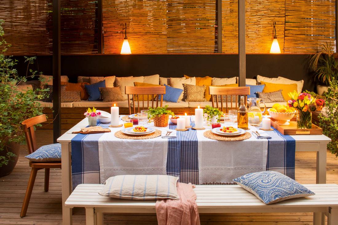 Comedor exterior con manteleria azul y blanco y cortinas de cañizo.