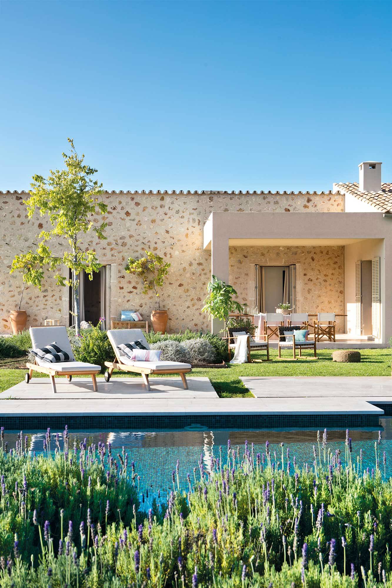 Jardín de una casa de piedra con piscina y porche de estilo moderno.