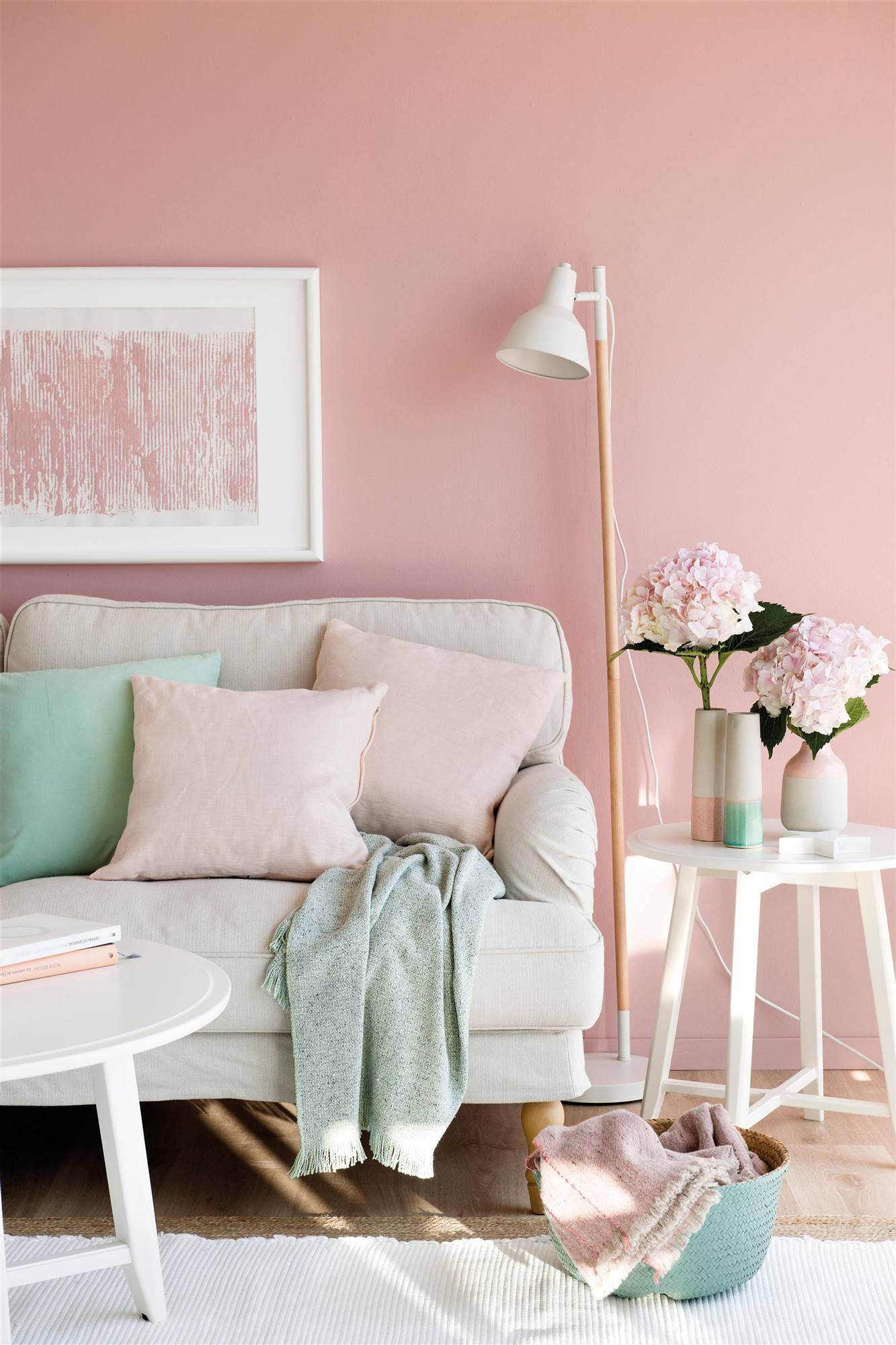 Salón con pared pintada de rosa, sofá blanco y detalles en azul. 