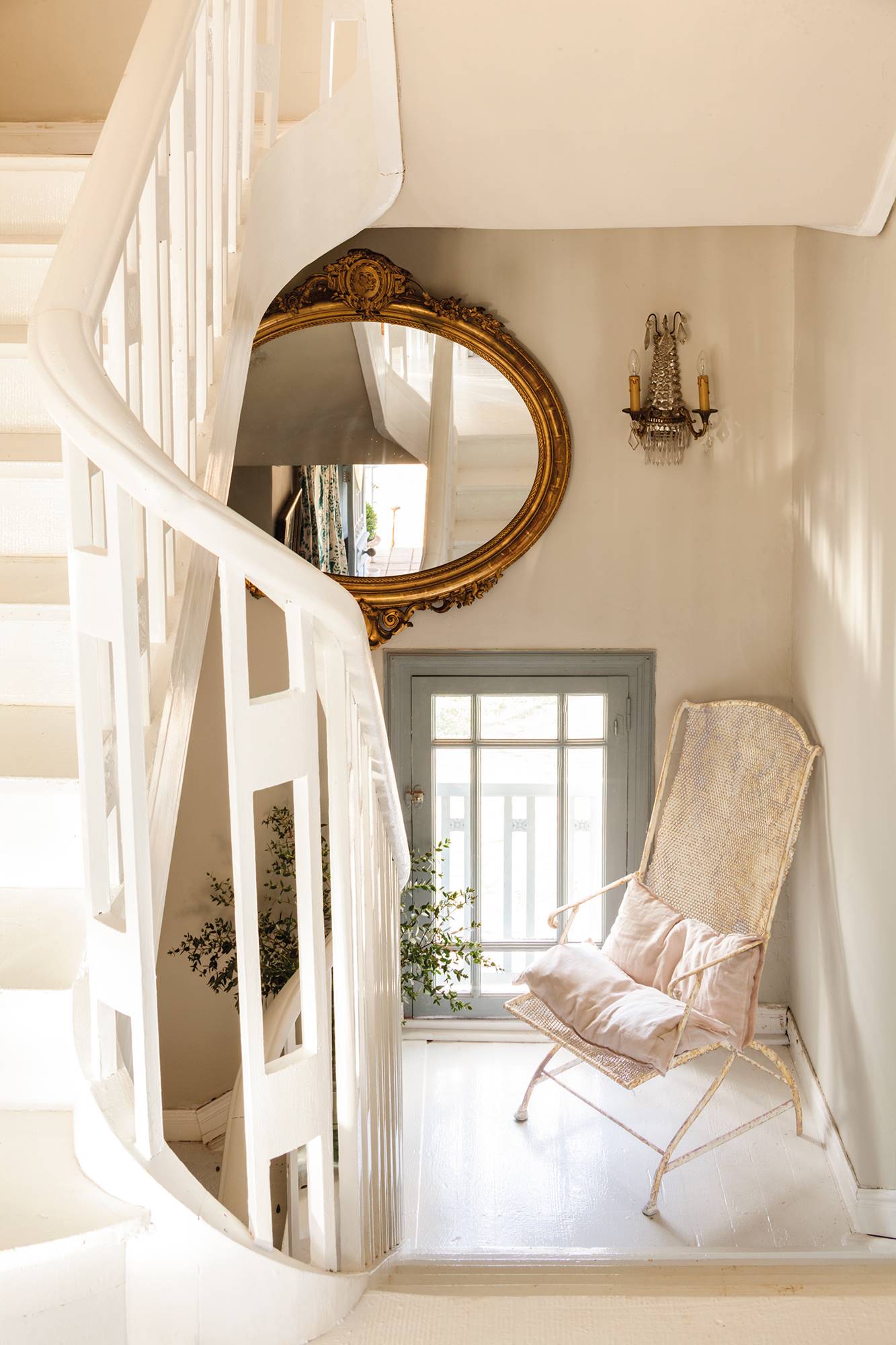 Escalera de madera blanca con silla de hierro blanca y espejo con marco dorado.