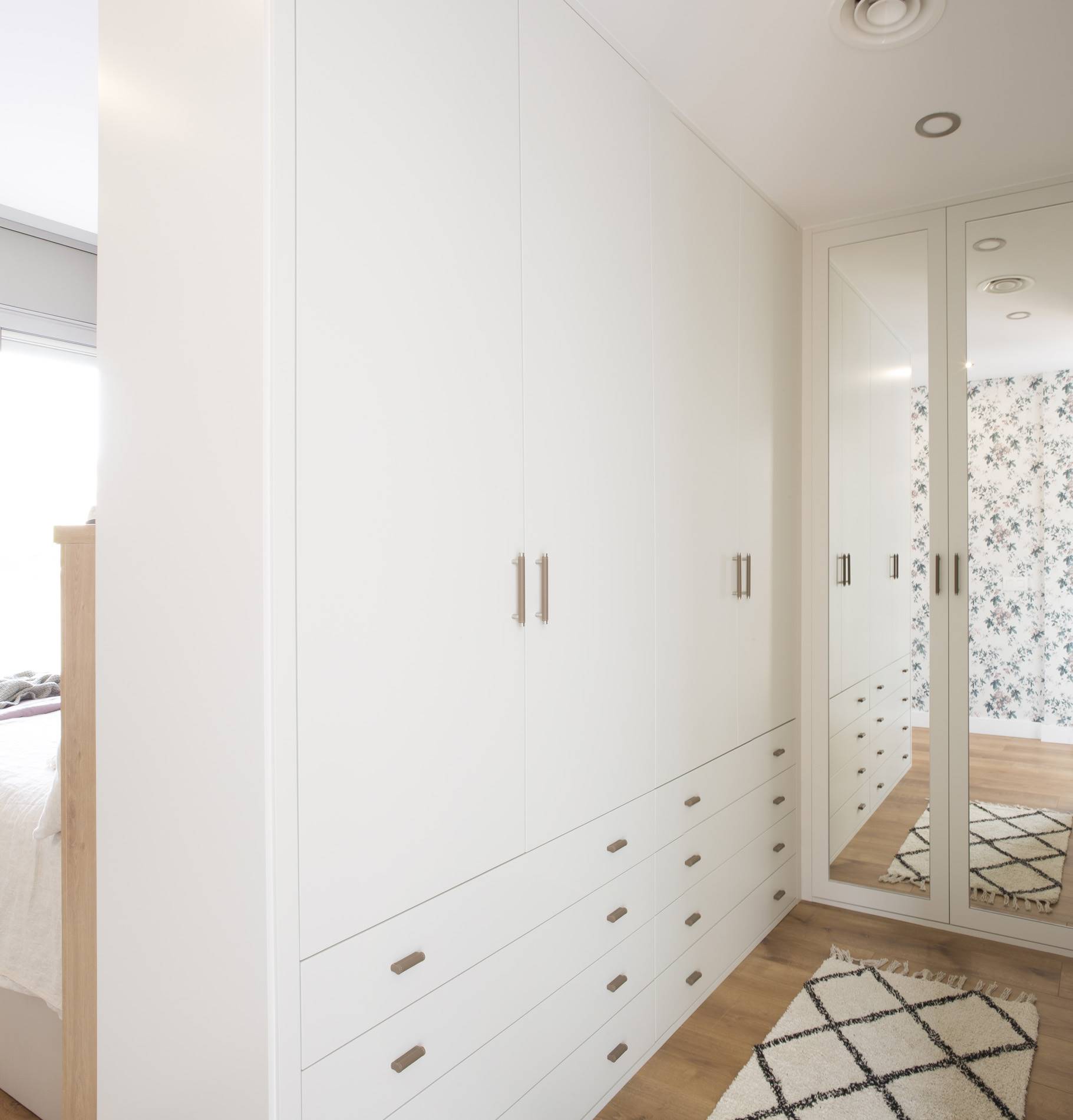 Vestidor con armarios blancos y puertas de espejo en una casa unifamiliar en Calafell proyecto de Pia Capdevila.