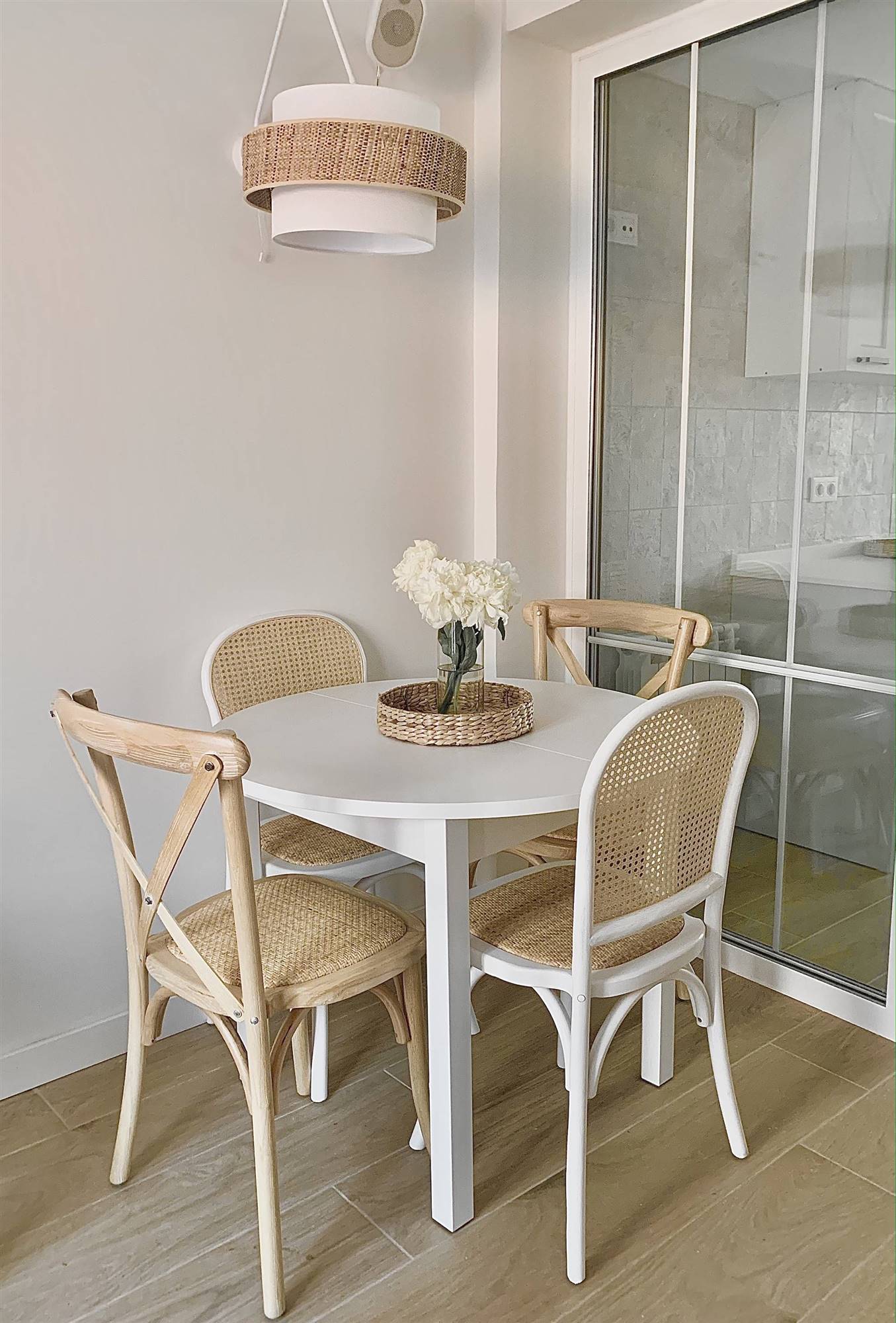 Comedor pequeño con mesa redonda en color blanco y con sillas de madera. 
