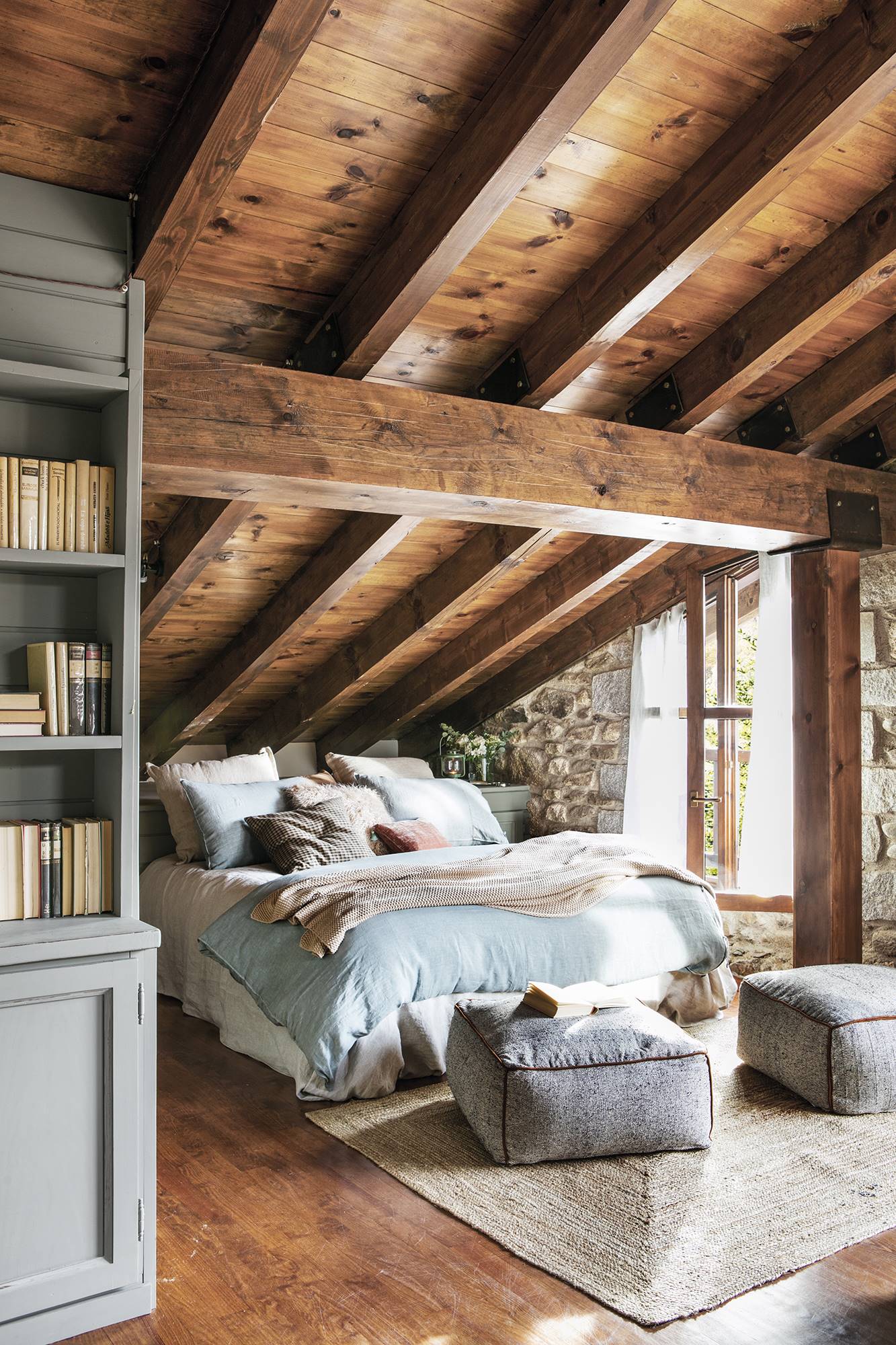 Dormitorio rústico con techos de madera abuhardillados y ropa de cama de lino. 