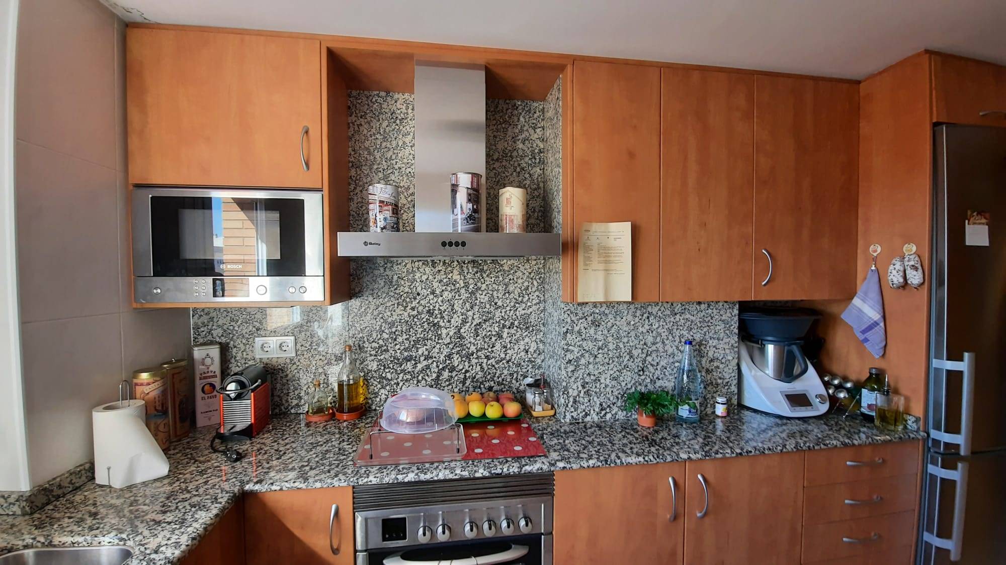 Zona para cocinar con armarios de madera, encimera de mármol y electrodomésticos a la vista.