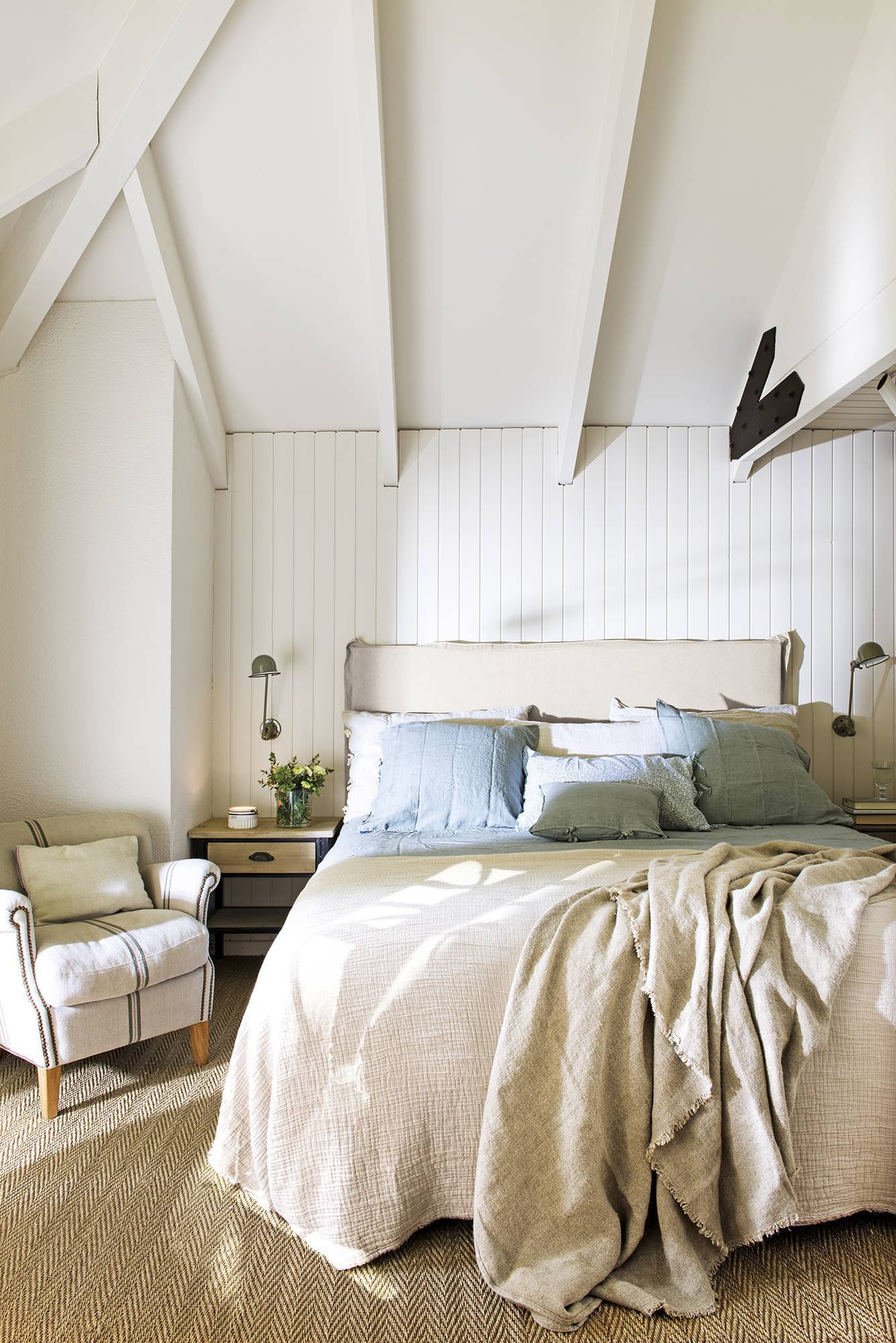 Dormitorio con paredes y techos panelados en madera pintada de blanca y ropa de cama blanca y azul. 