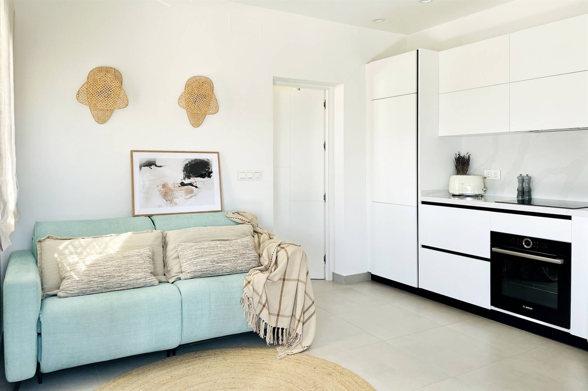 Pequeño salón moderno junto a la cocina abierta con mobiliario en color blanco.