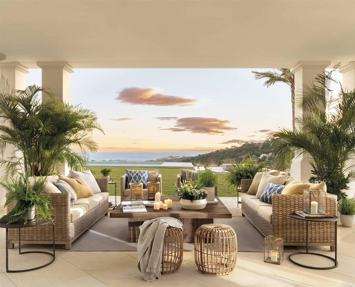 Un porche con salón exterior y comedor con vistas al mar en Marbella y muebles de fibras naturales. 