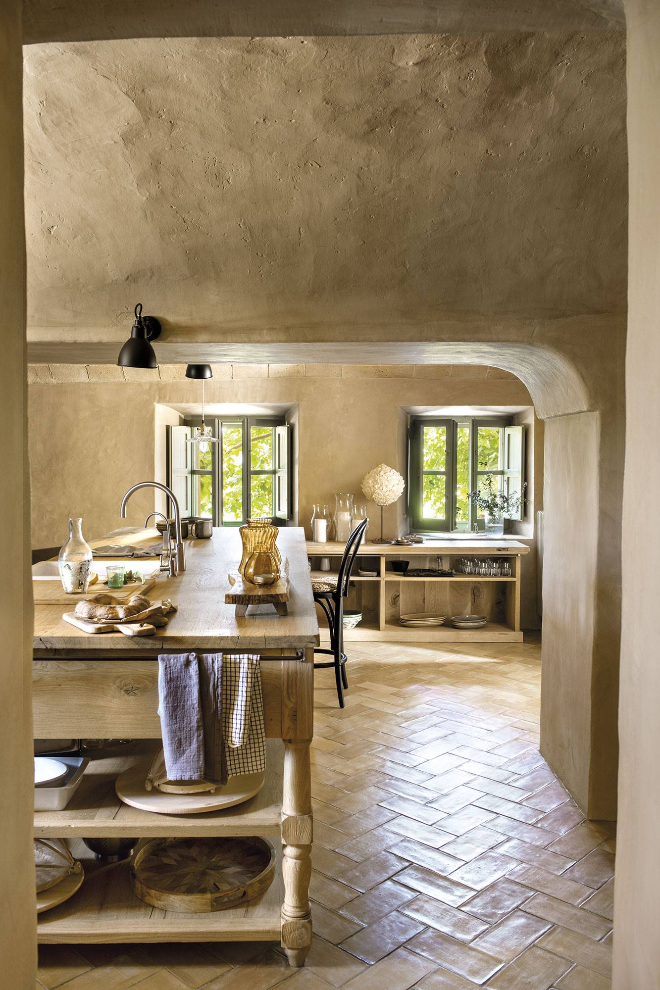 Cocina con suelo de barro, muebles de madera y ventanas verdes