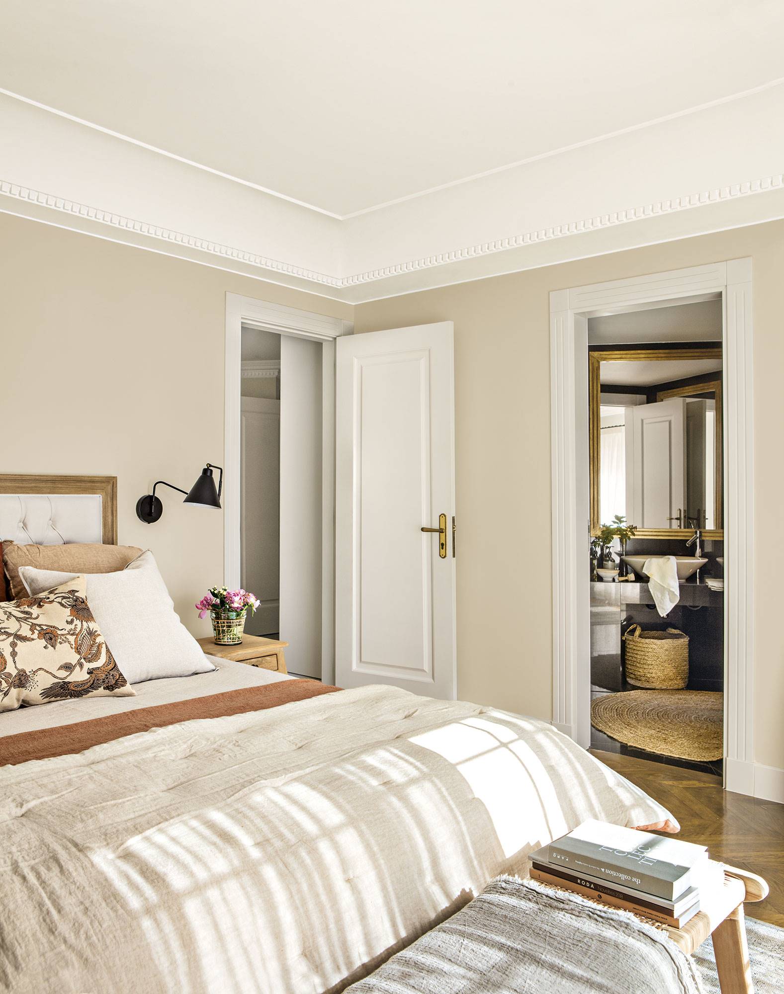 Dormitorio principal con cama decorada en tonos tierra, banqueta y baño privado.