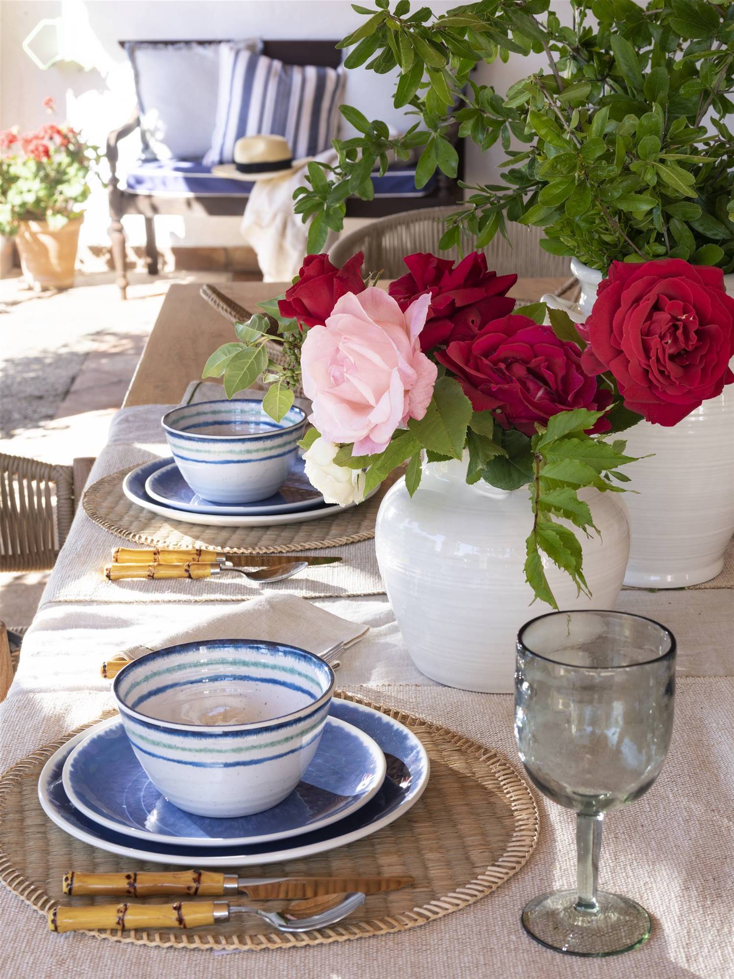 Mesa de verano con vajilla azul y jarrón con flores. 