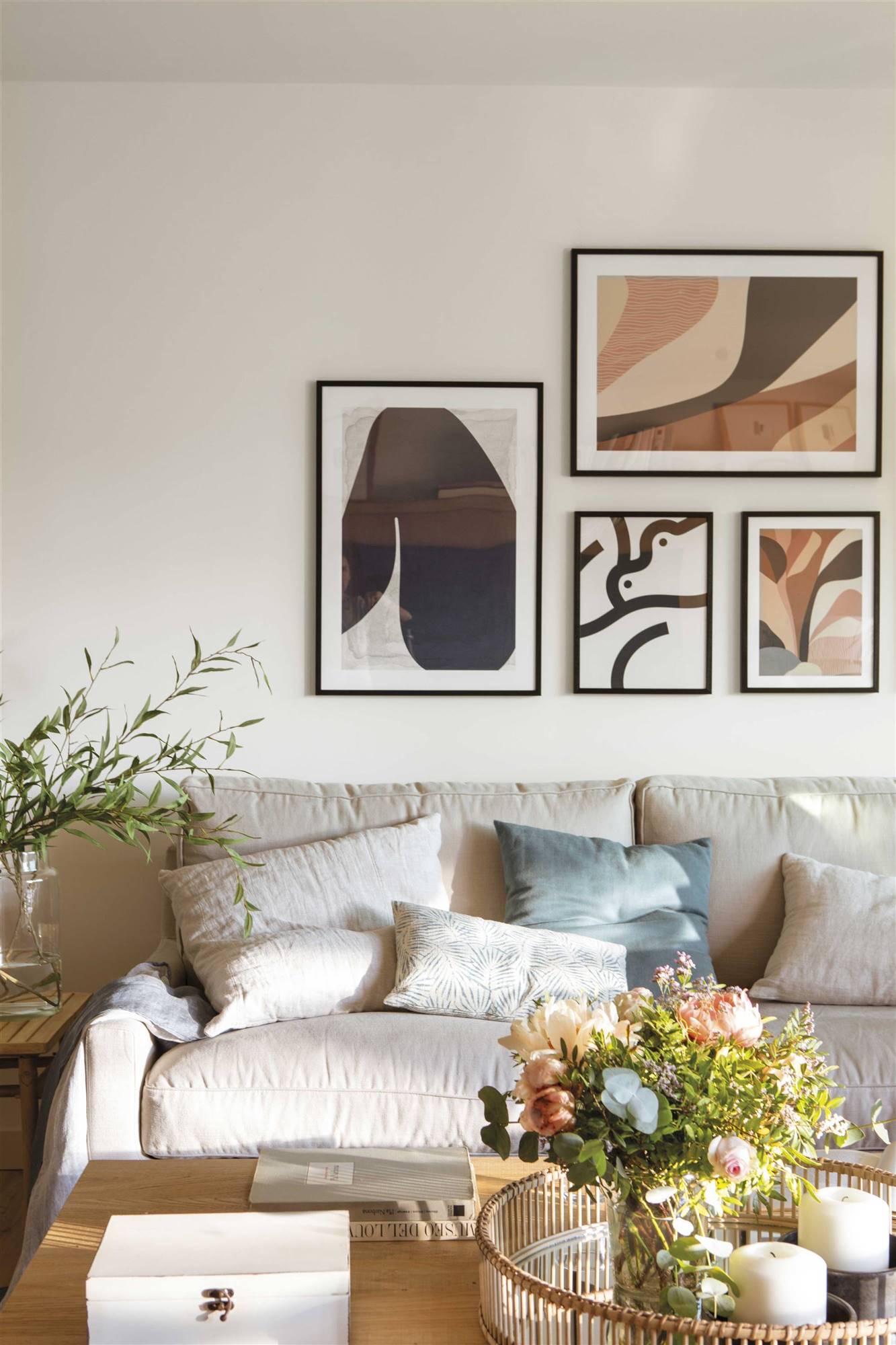 Detalle de salón con sofá beige y cojines y mesa de centro con flores. 