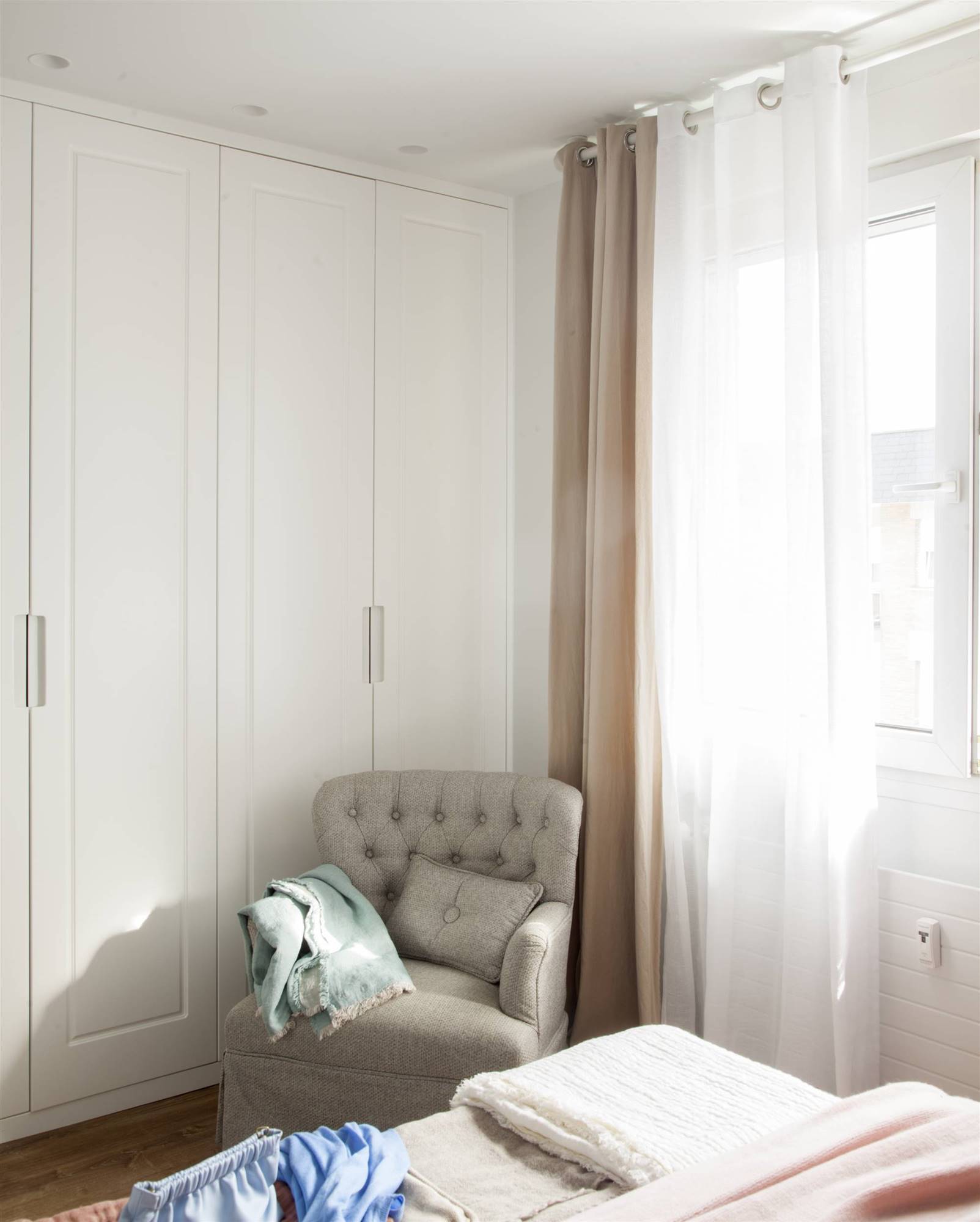 Dormitorio con armario blanco y butaca.