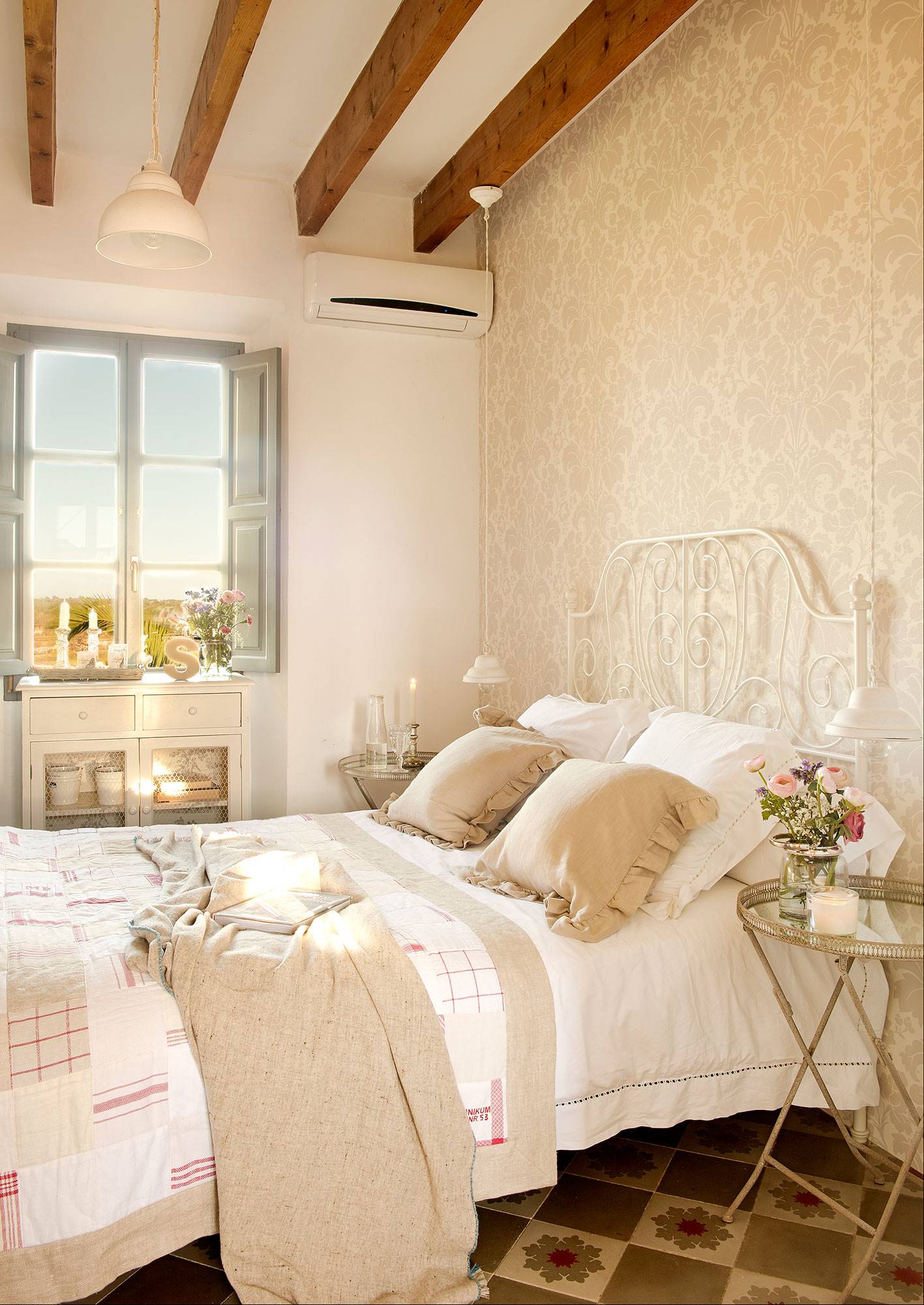 Dormitorio vintage con cama de forja blanca y papel pintado en la pared del cabecero con estampado floral. 