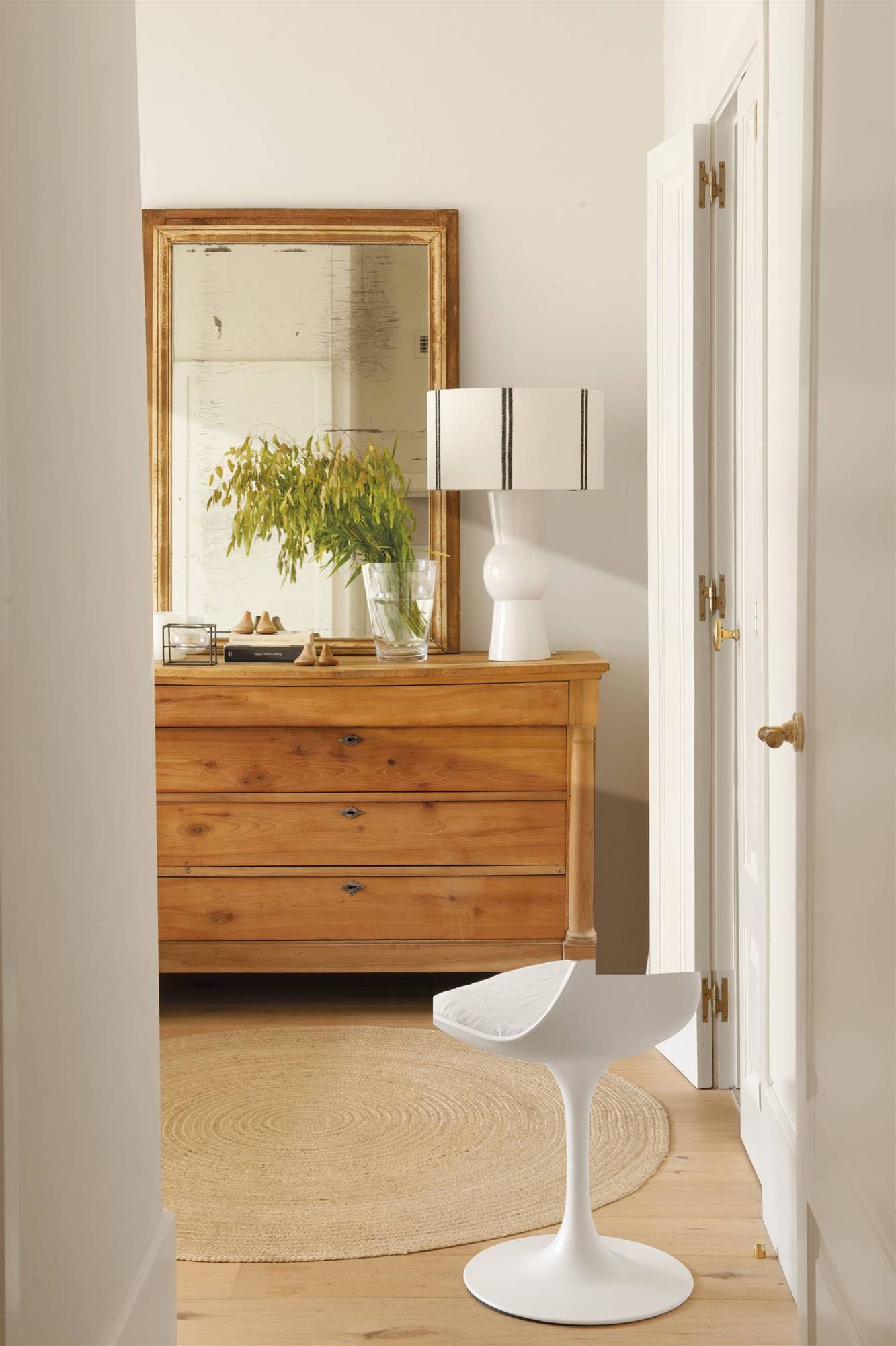 Cómoda con espejo antiguo encima y silla blanca moderna. 