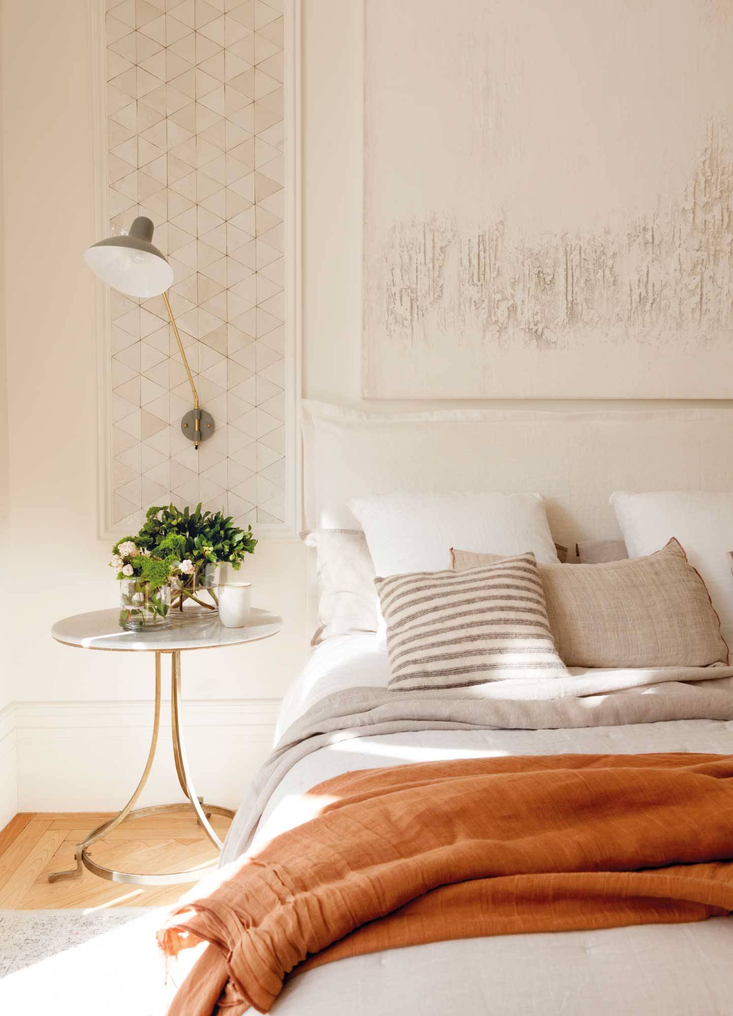 Dormitorio con ropa de cama de tonos anaranjados y pared en color piedra suave. 