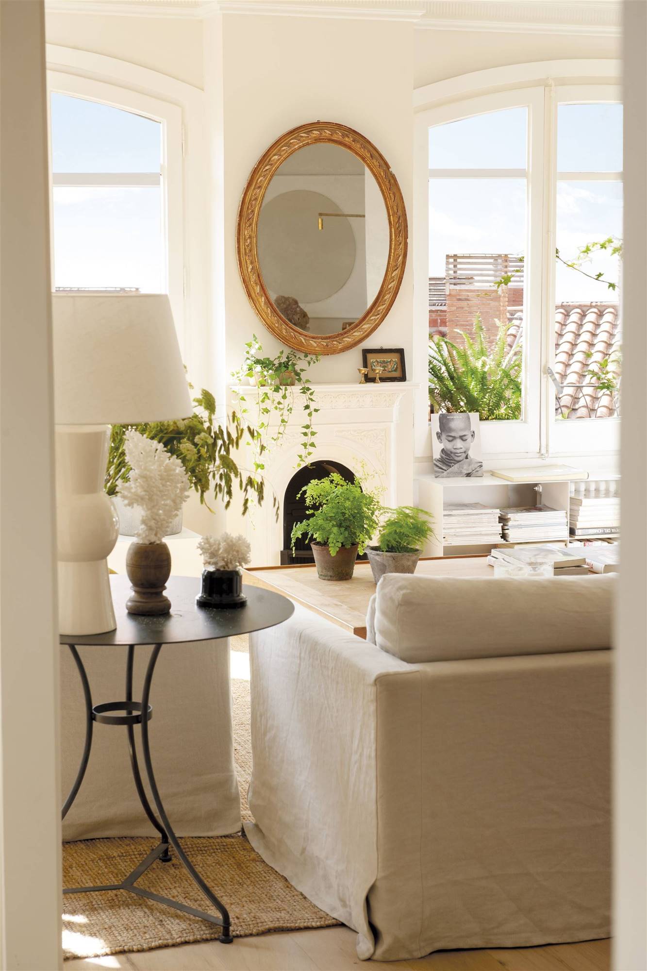 Salón con espejo redondo sobre la chimenea y sofá a medida en blanco. 