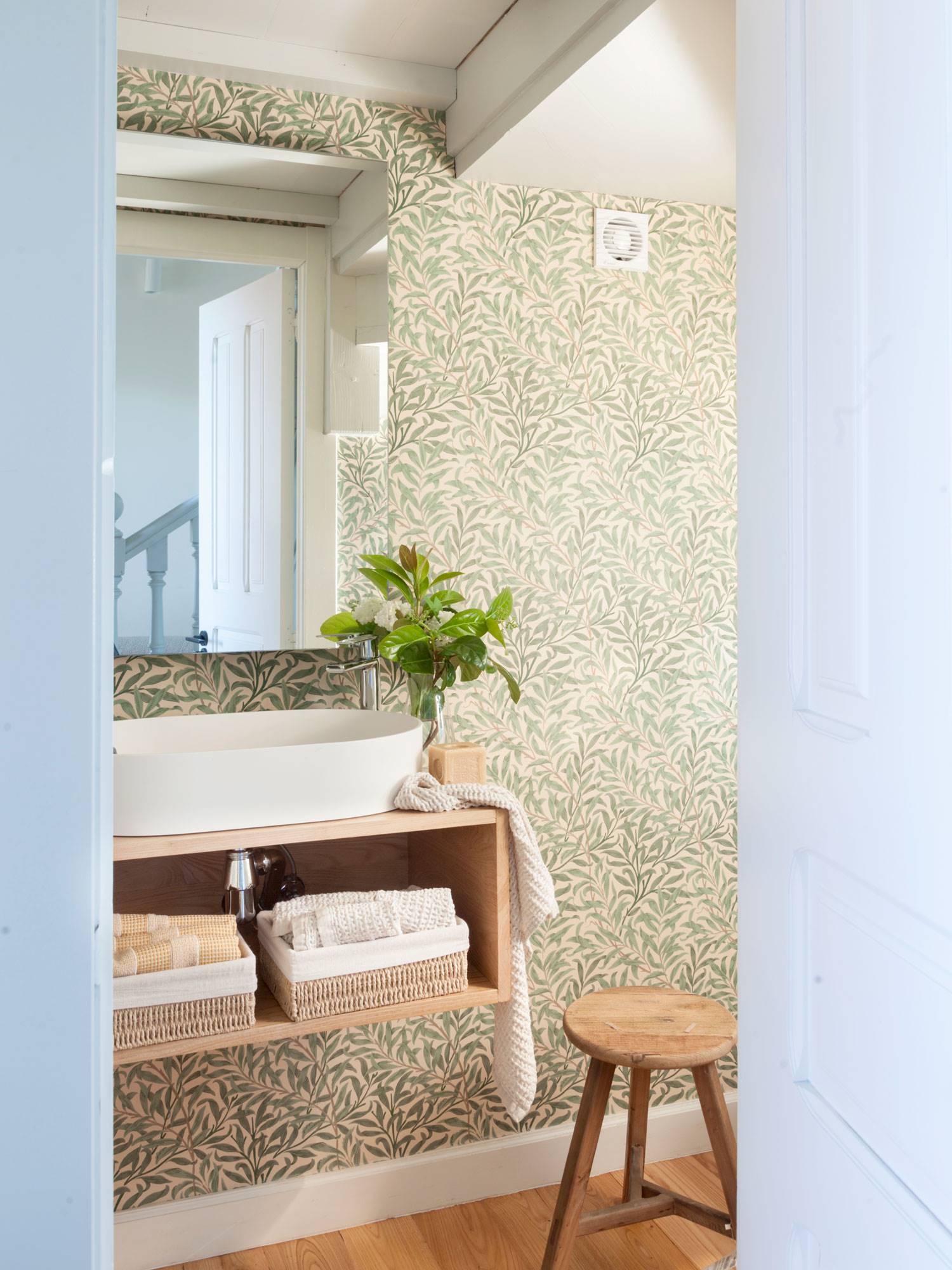 Baño con papel pintado estampado floral y mueble suspendido de madera. 