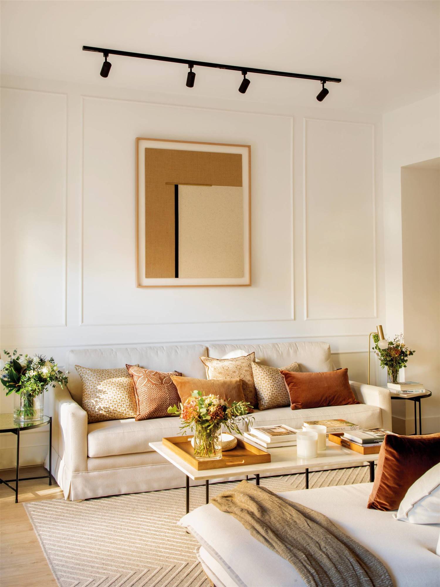 Salón con sofá blanco, molduras en pared y cuadro en tonos neutros