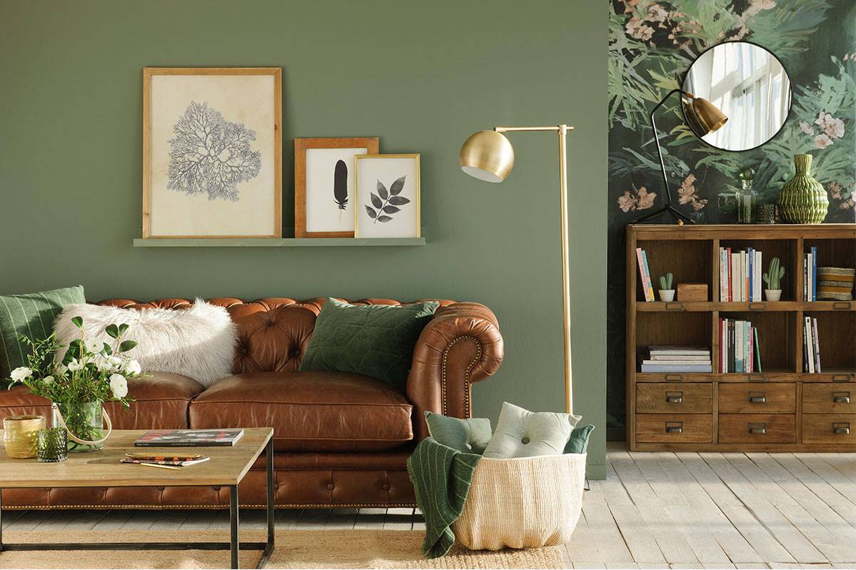 Salón con sofá chéster de cuero y pared pintada de verde. 