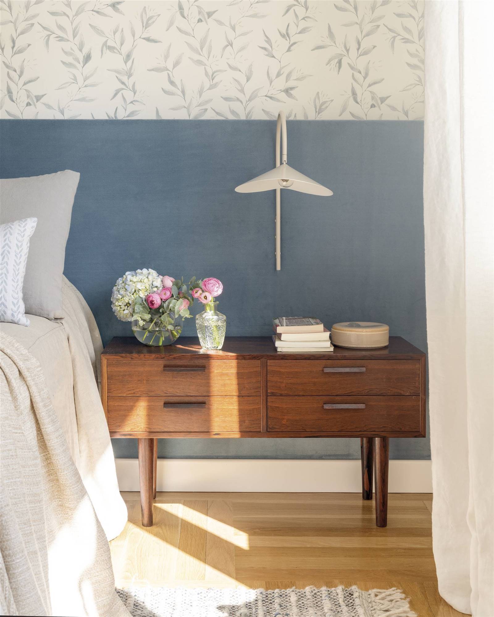 Dormitorio con cabecero azul, papel pintado de flores y mesita de noche de los años 50. 