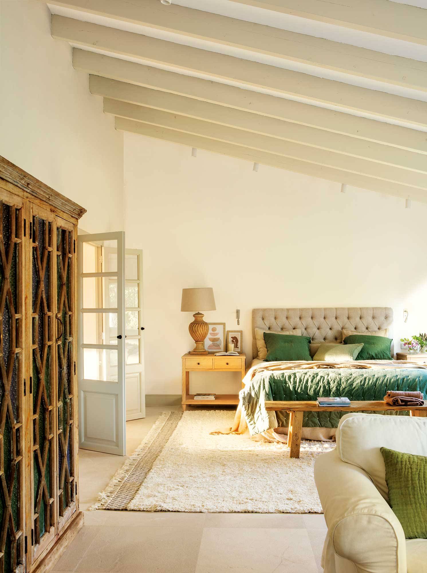 Dormitorio blanco con armario de madera y cabecero tapizado con capitoné en beige. 