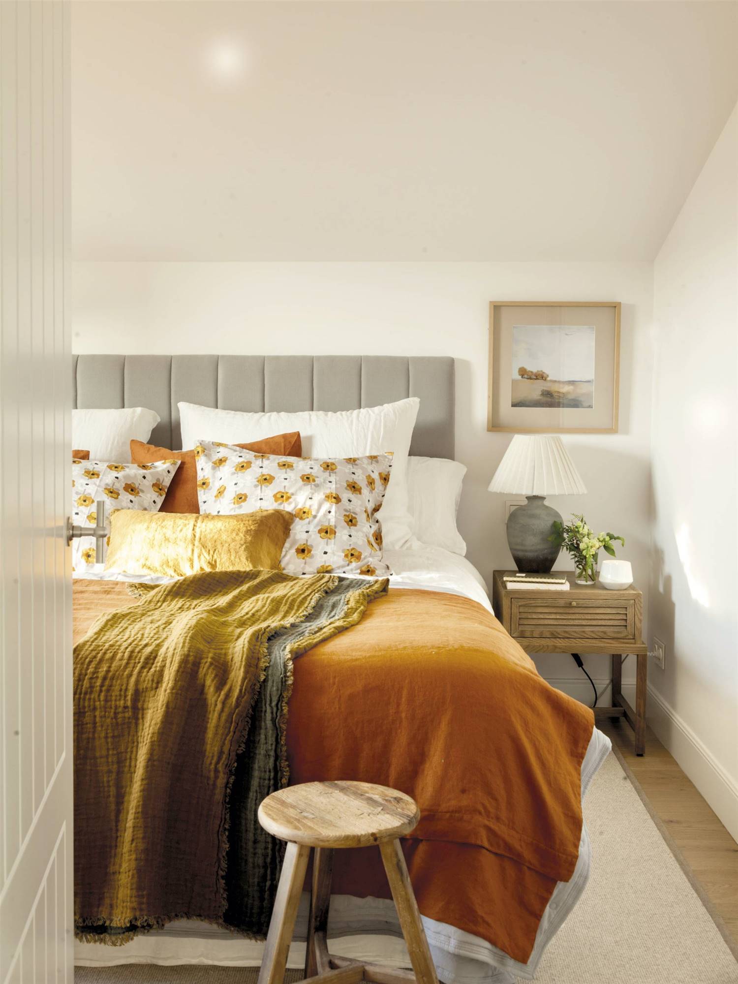 Dormitorio blanco con cabecero gris y ropa de cama en tonos ocres. 