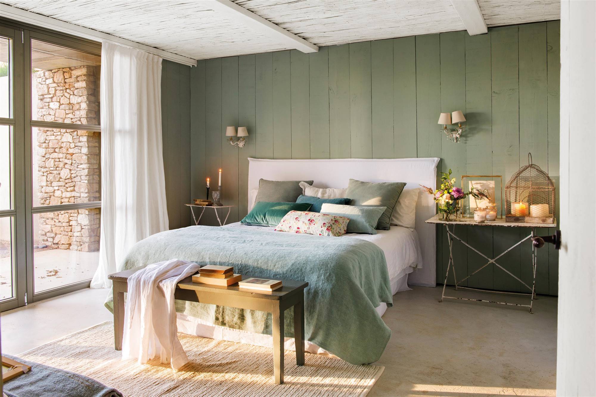Dormitorio con pared revestida de madera en verde grisáceo y cabecero tapizado en blanco. 