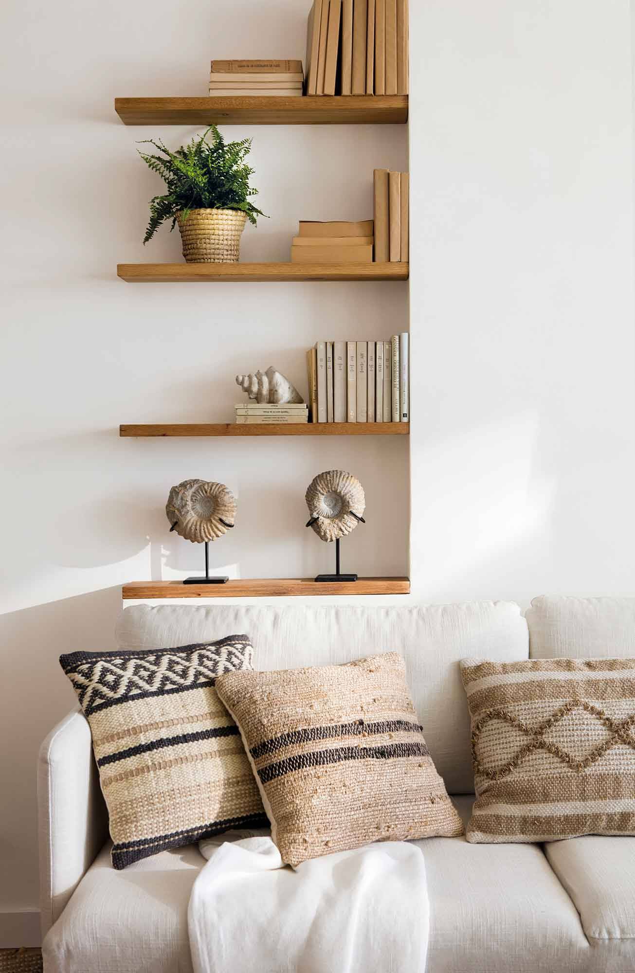 Salón con sofá blanco, cojines beiges y estantes de pared