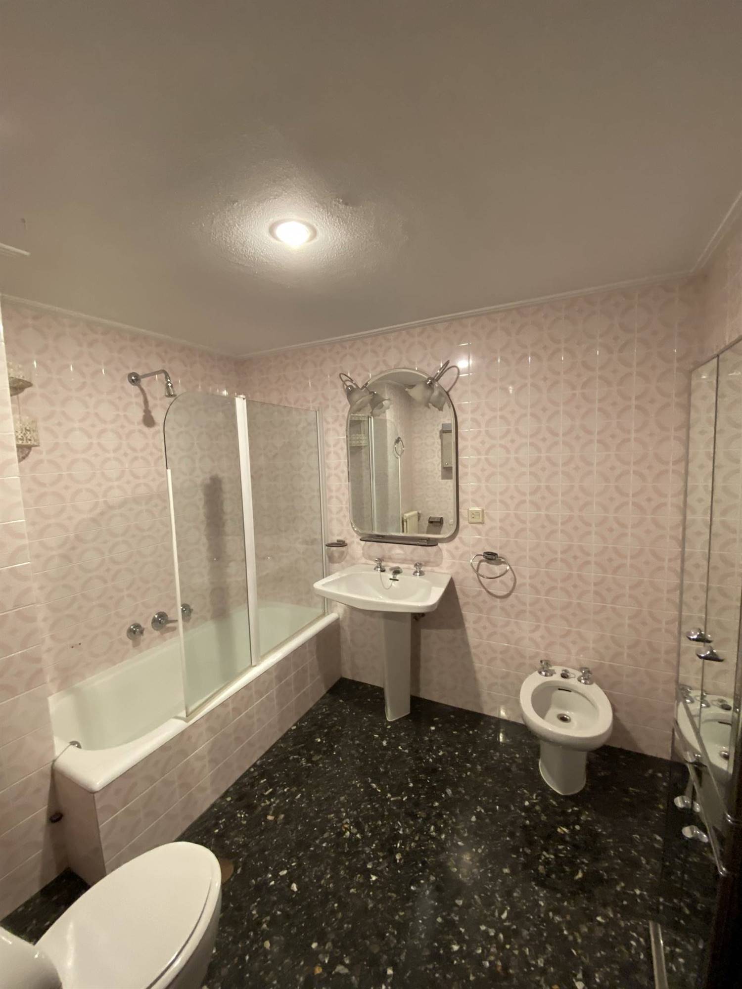 Un baño antiguo con azulejos en rosa y suelo negro tipo terrazo.