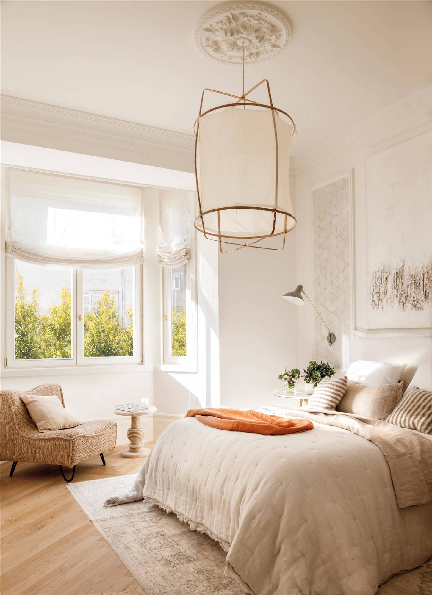 Dormitorio clásico blanco con gran lámpara, molduras y una butaca. 