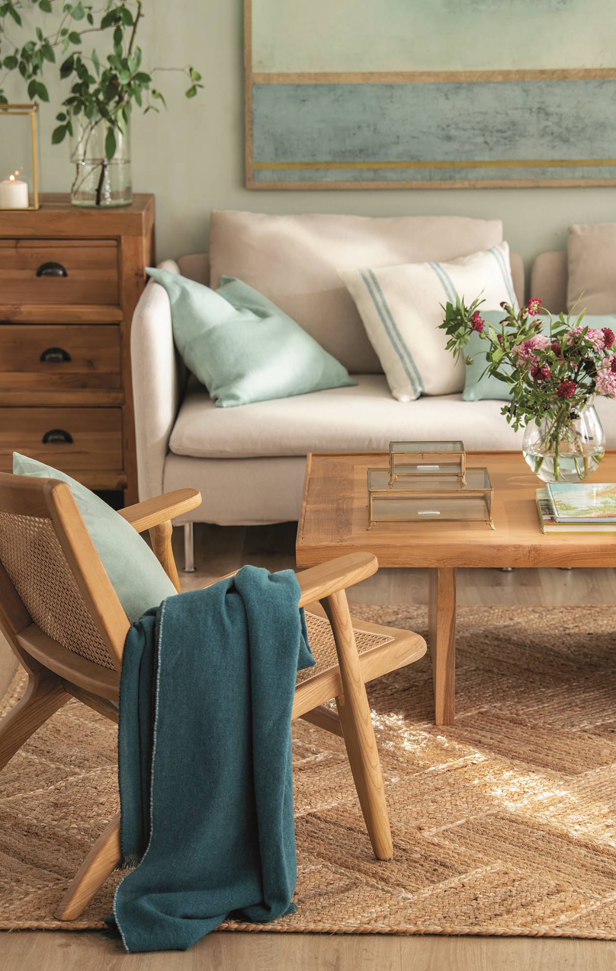 Salón con mesa de centro, butaca de madera y sofá gris sobre alfombra de fibras naturales.