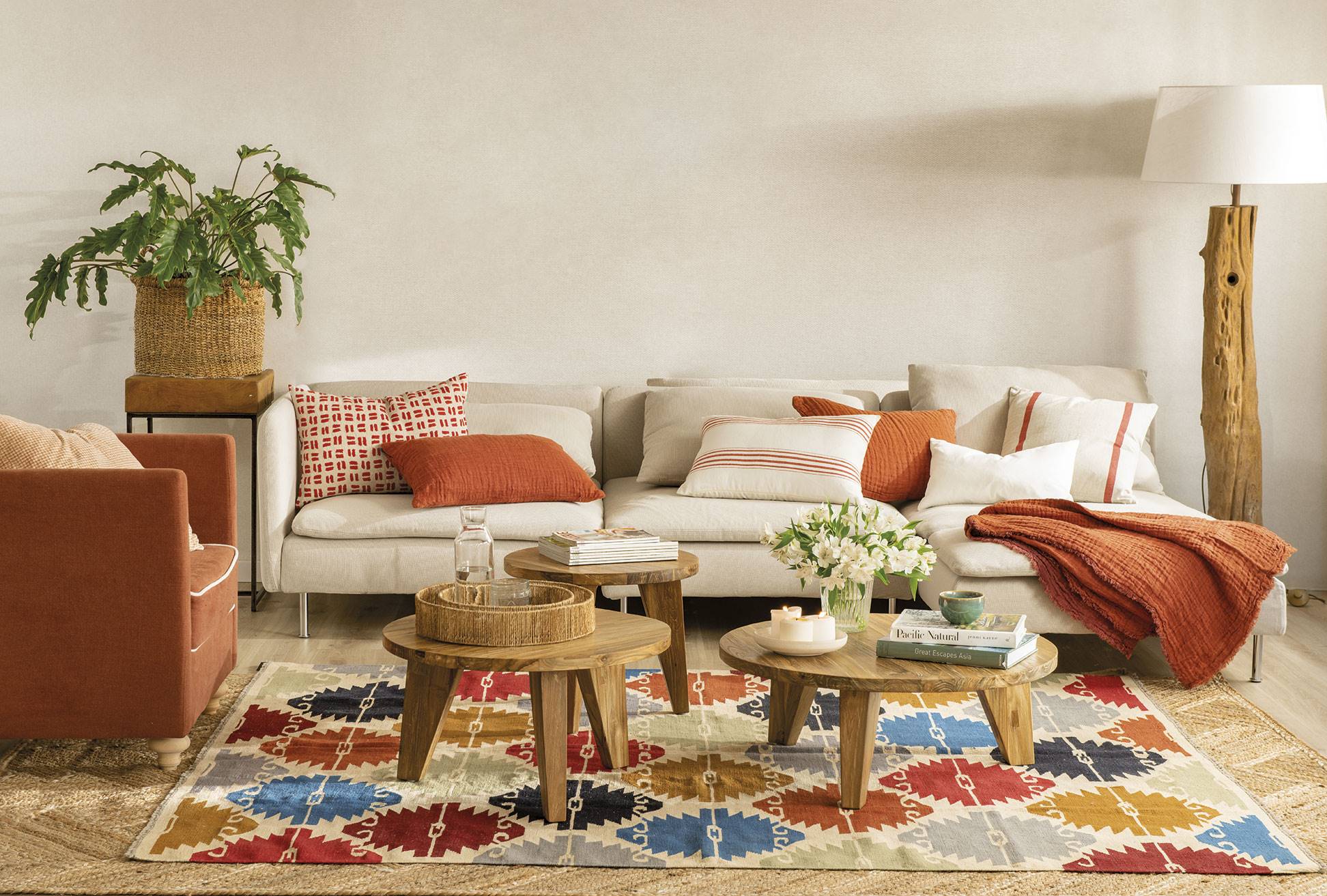 Salón con sofá, butaca y textiles en color teja, tres mesas de centro de madera y alfombra kilim con rombos de colores.