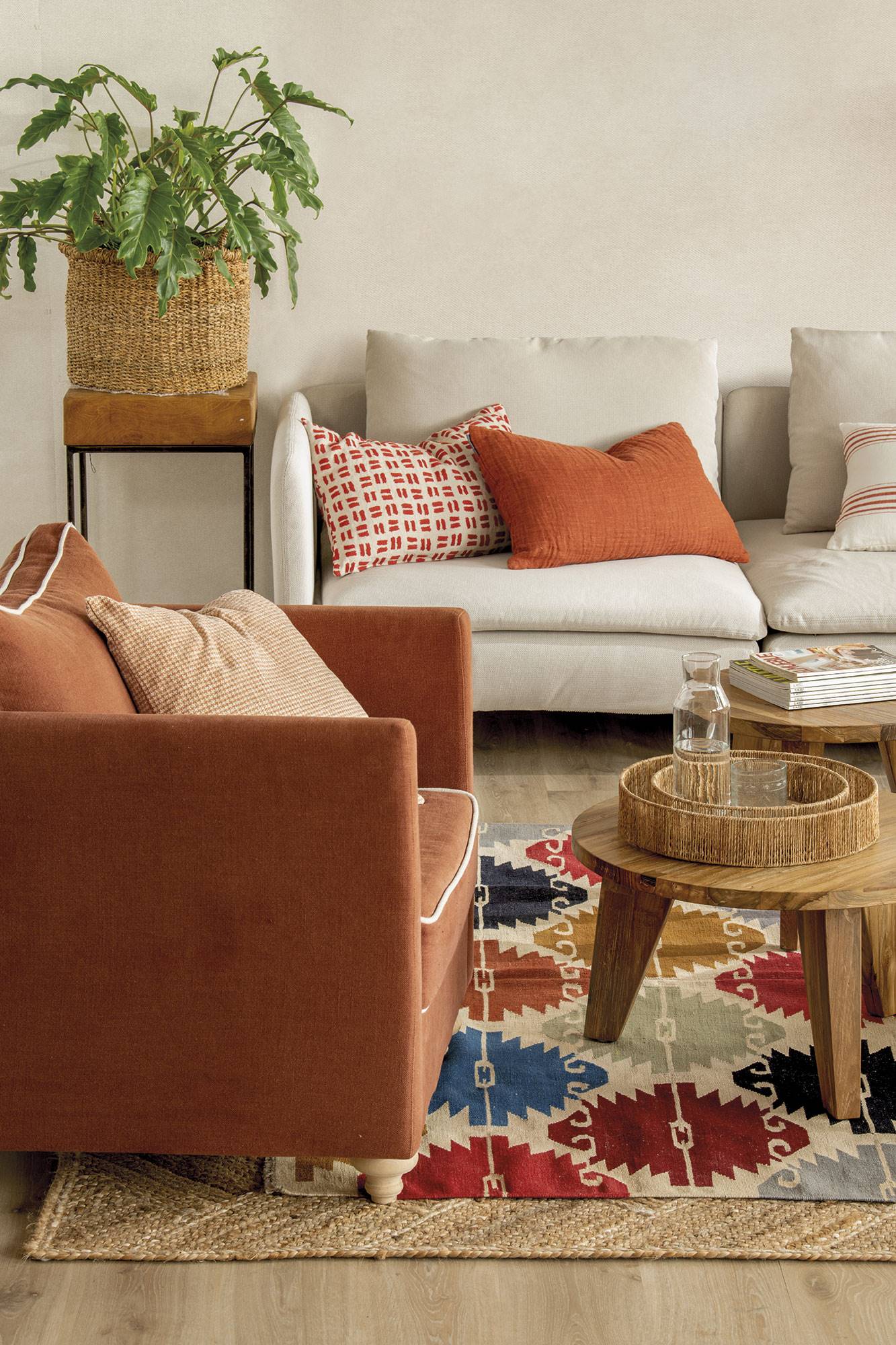 Butaca teja sobre alfombra de fibras y kilim con rombos de colores, mesas de centro de madera y sofá tapizado en blanco.