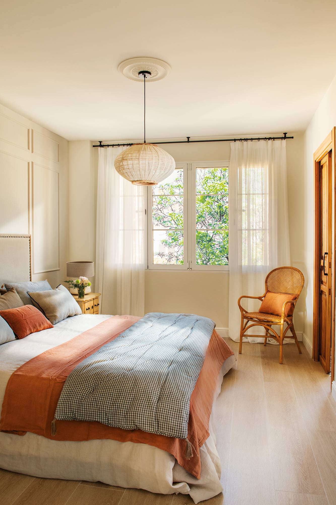 Dormitorio decorado con lámpara de techo y butaca y cama rematada con plaid acolchado.