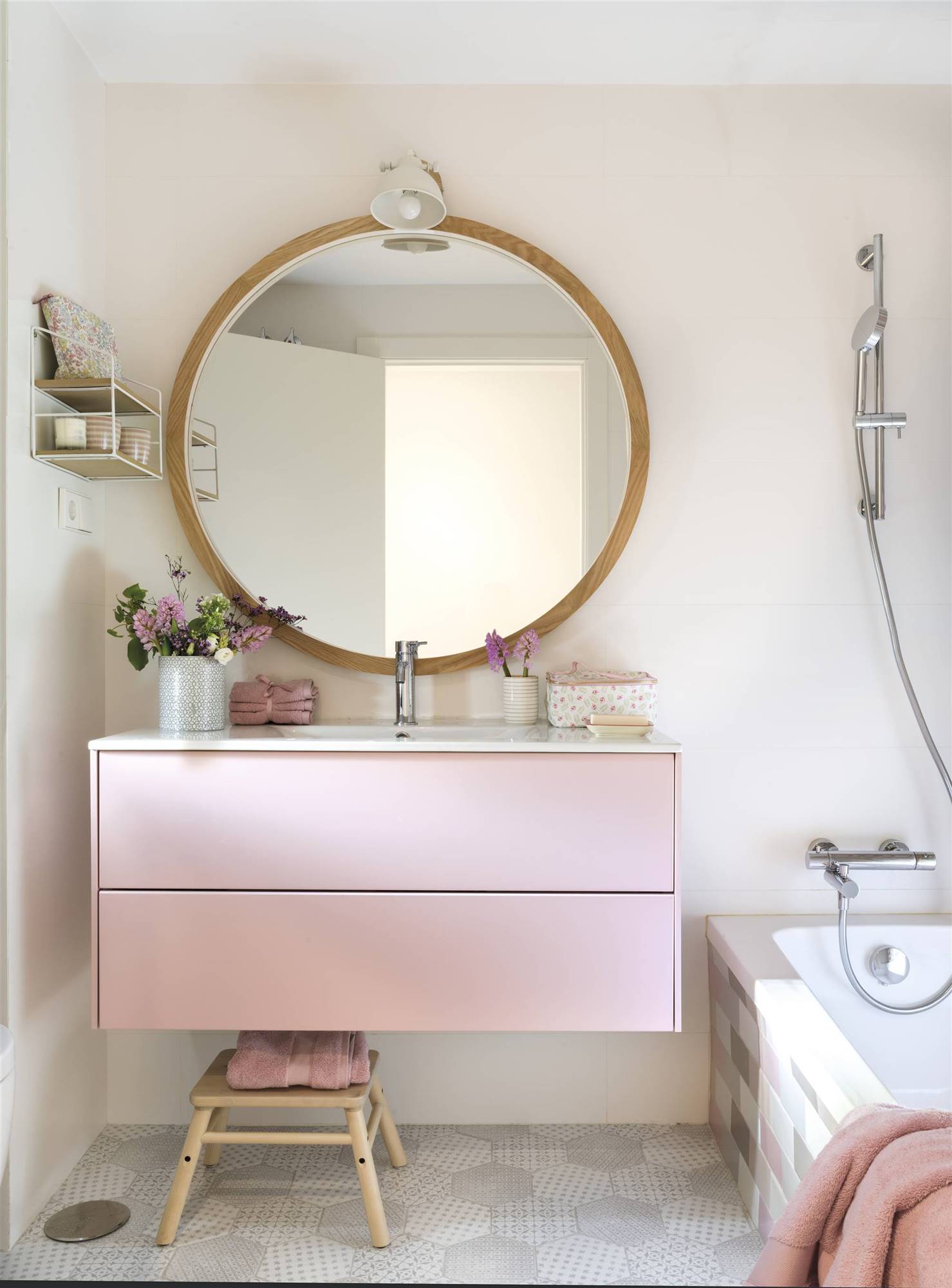 Baño con mueble rosa y espejo redondo. 