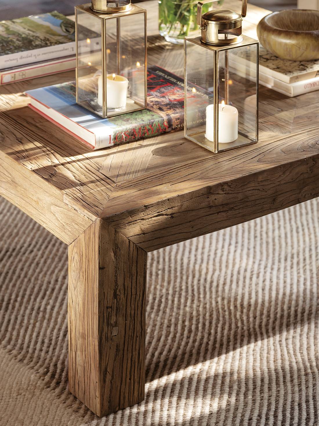 Una mesa de centro de madera reciclada con faroles dorados y una alfombra de lana y algodón.